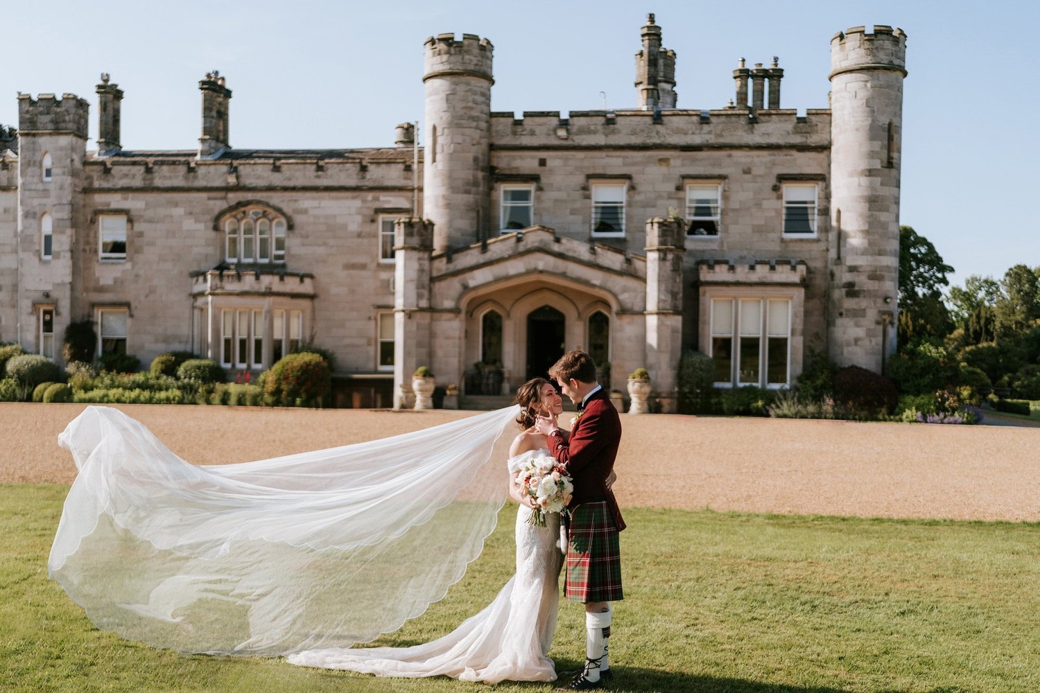Kim and Kenneth embracing on the lawn in front of Dundas Castle, with Kim’s veil flowing beside them.