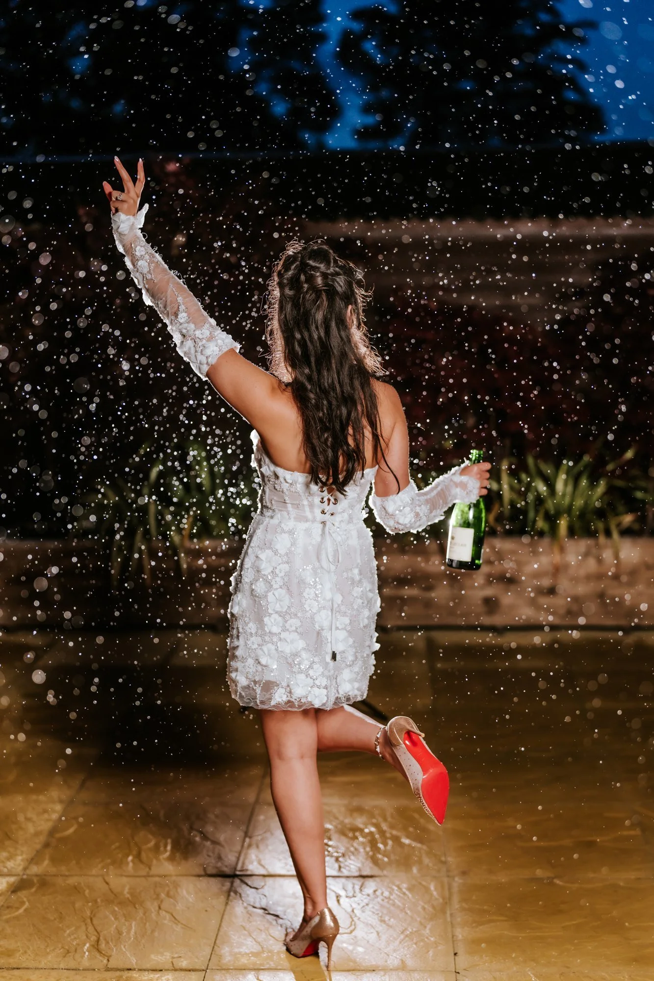 Kaitlyn raising a peace sign in the rain with a champagne bottle in her hand at Glenbervie House.