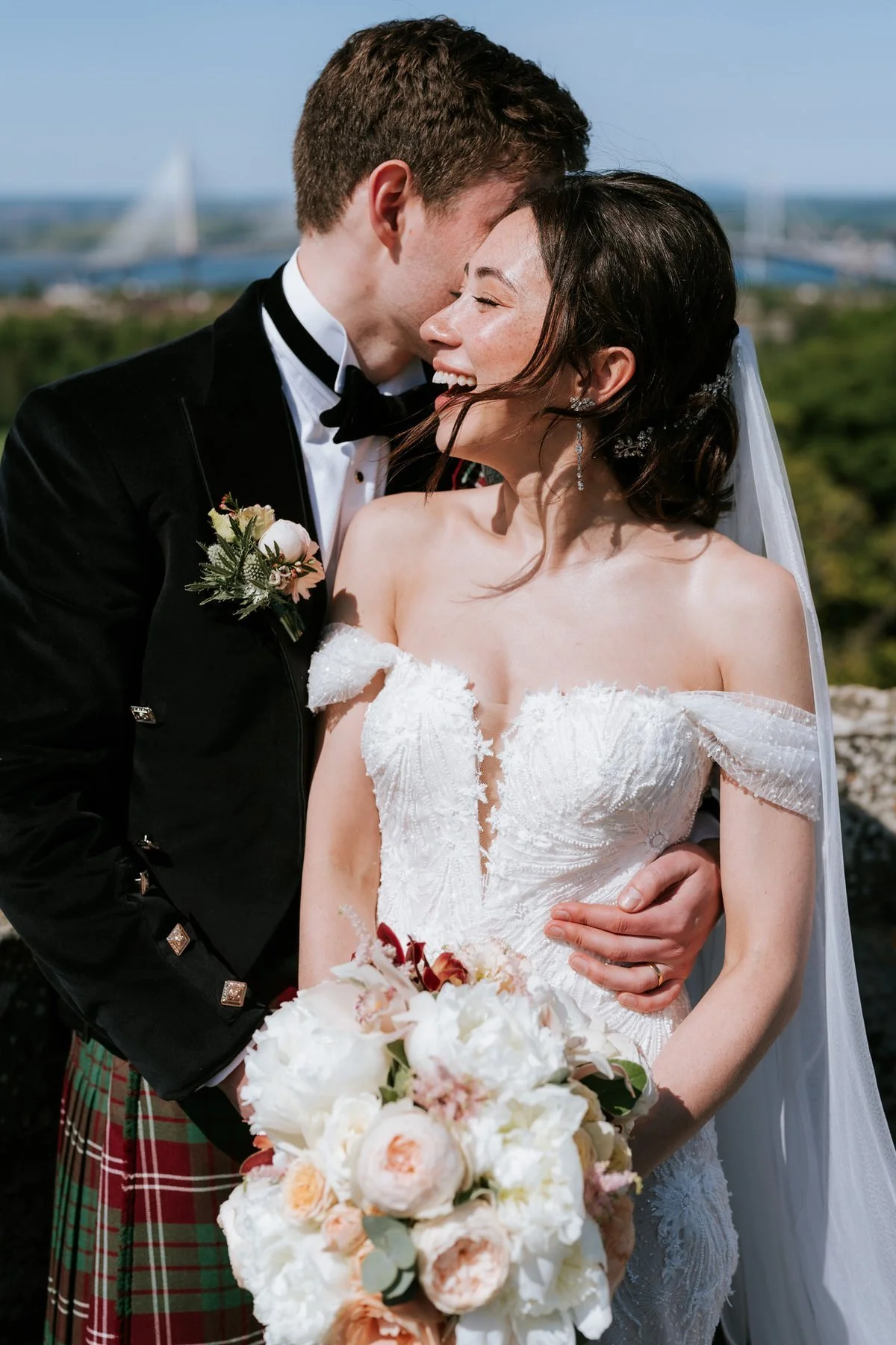 Kenneth kissing Kim on the forehead on the castle rooftop, with the Forth crossings behind them.