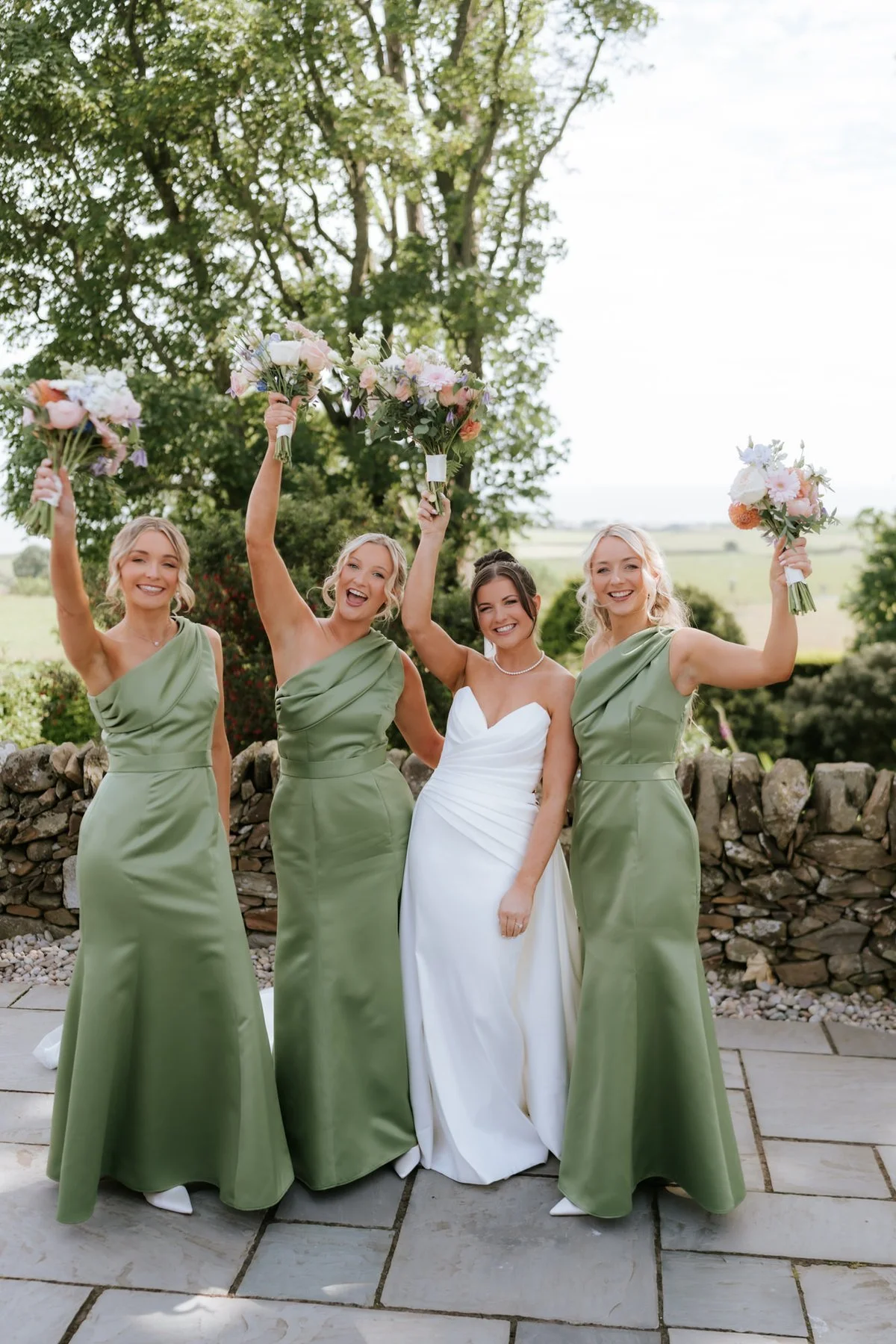 Lois and her three bridesmaids raising their bouquets outside GG’s Yard.