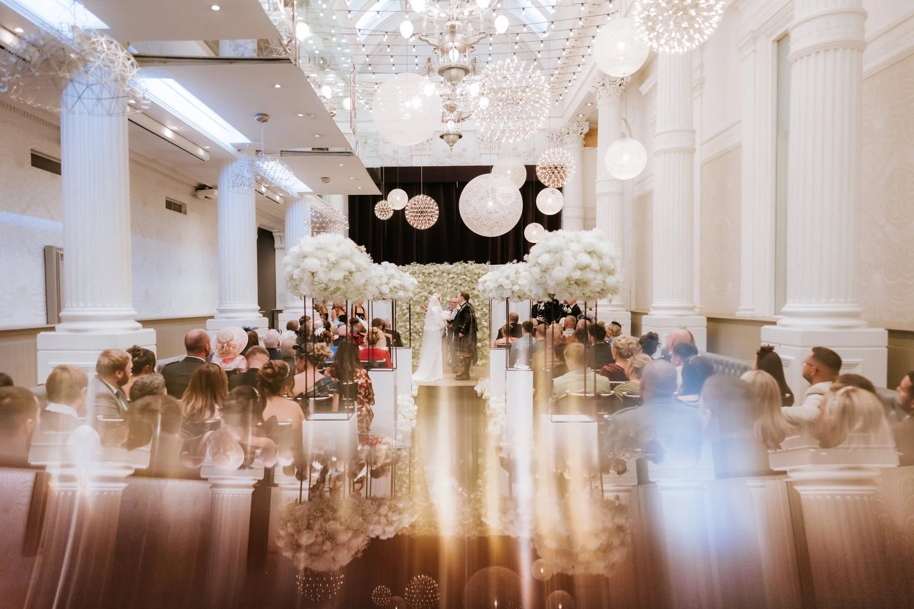 A wide view of the flower-lined aisle and globe lights during the Corinthian wedding ceremony.