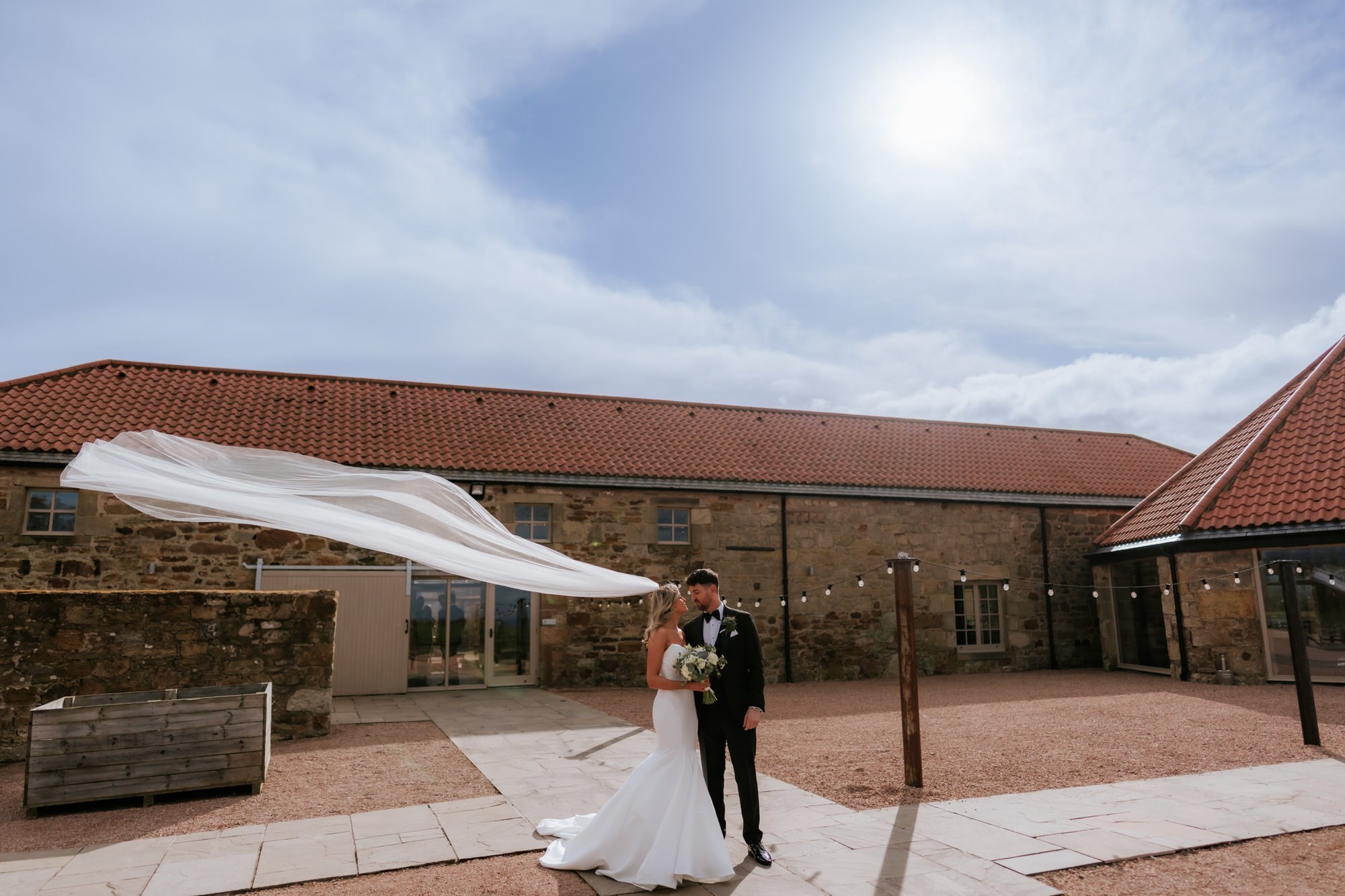 Natalie and Jamie standing together beneath her windblown veil