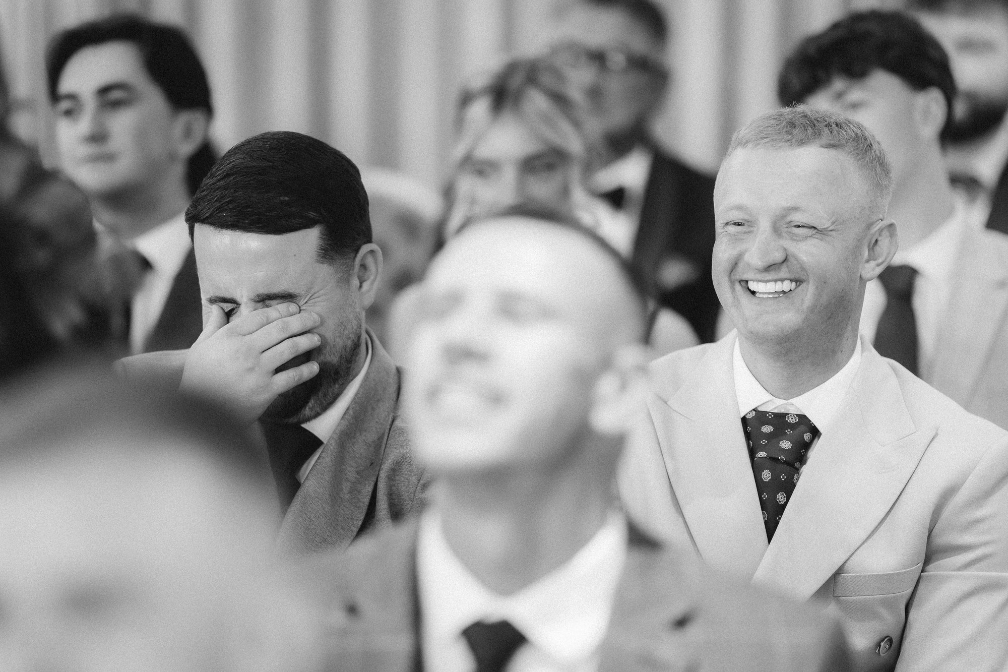 Wedding guests laughing during the ceremony in black and white.