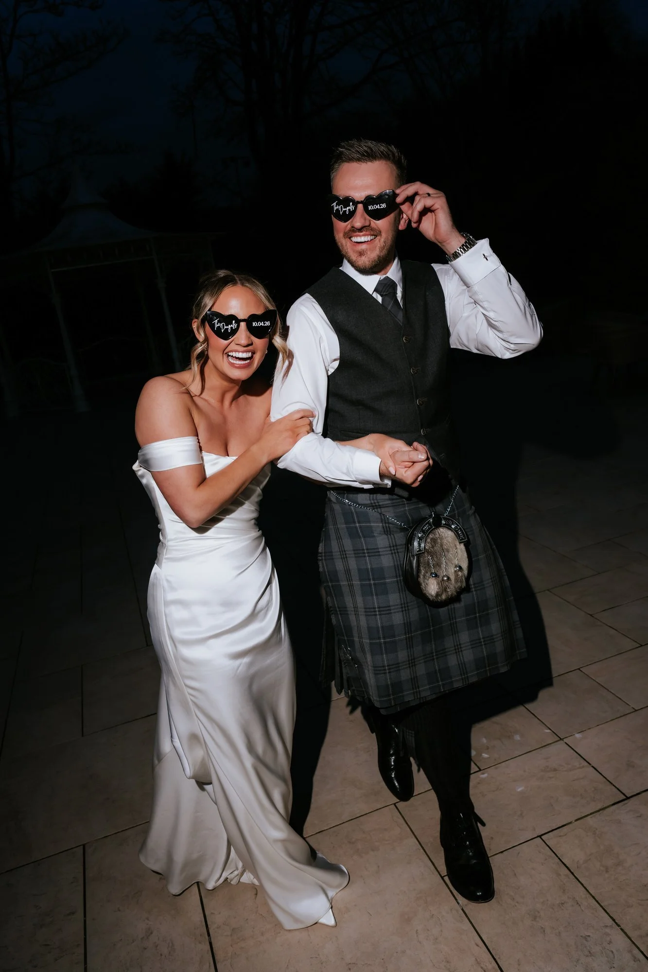 Elle holding Adam's arm as they laugh together outside after dark