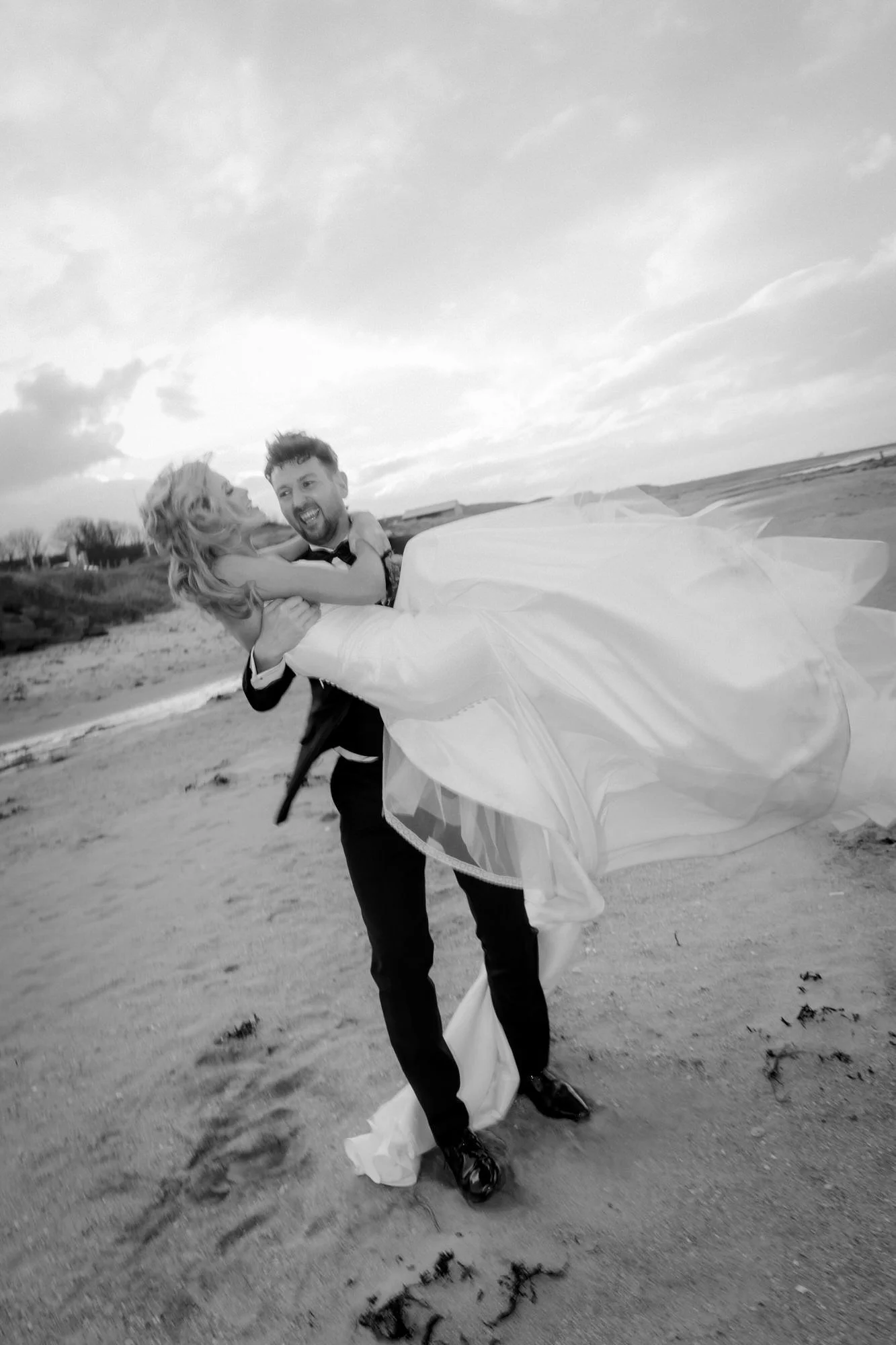 Jamie carrying a laughing Natalie on Kingsbarns beach, in black and white