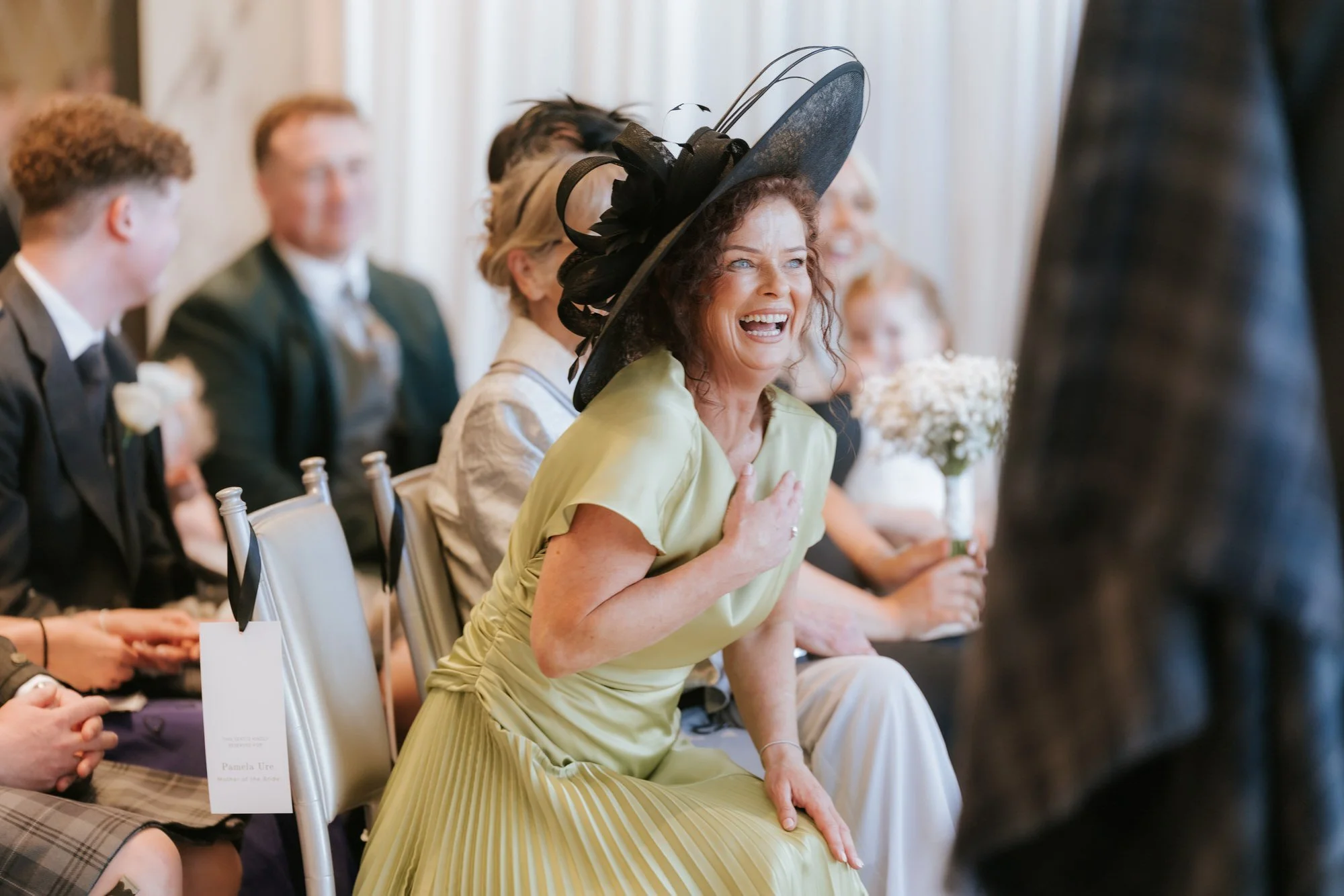A guest in a lime dress laughing with her hand against her chest