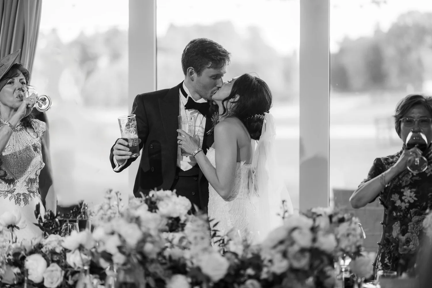 Kim kissing Kenneth while holding a drink during the wedding reception, photographed in black and white.
