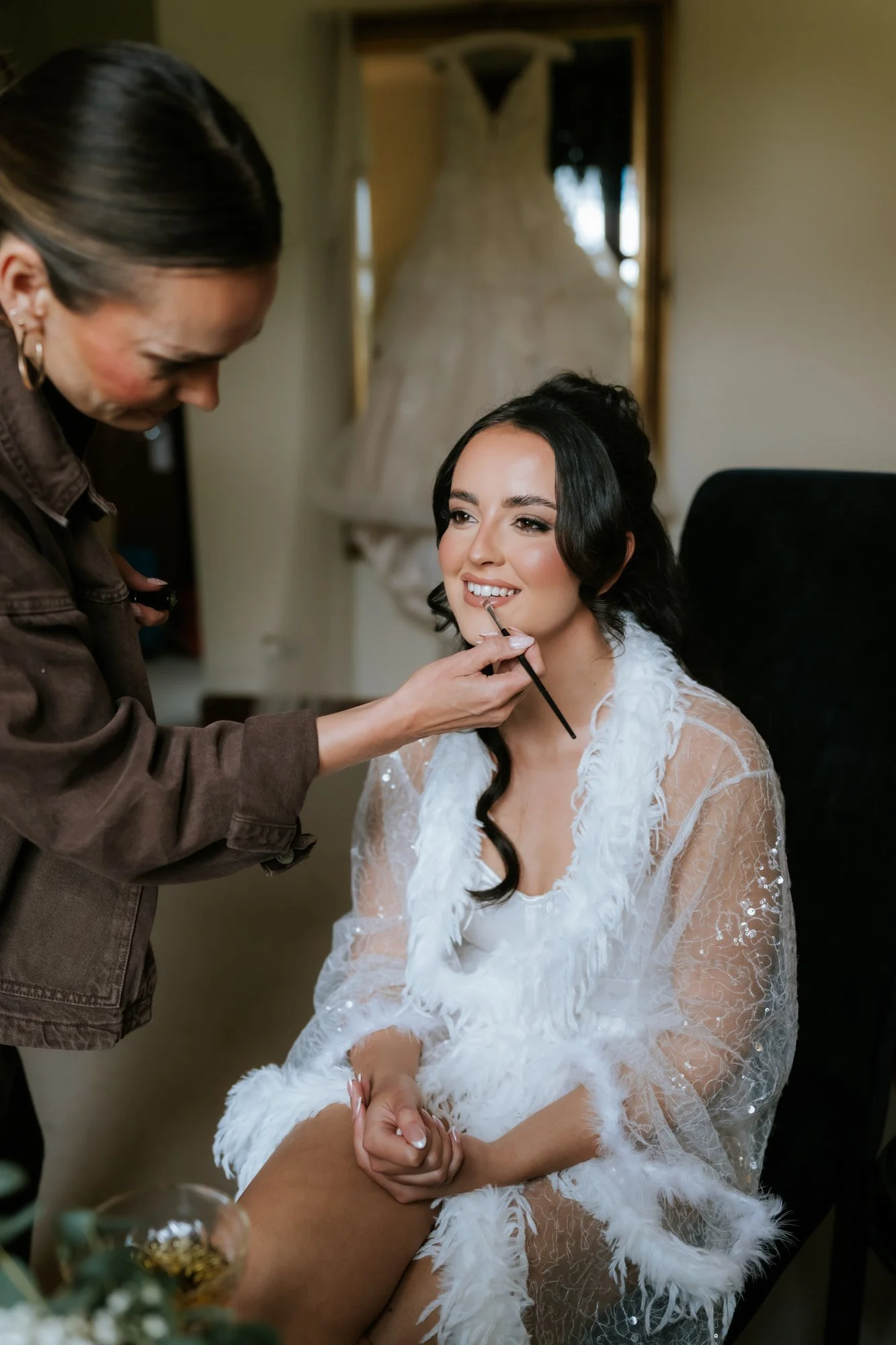 Kaitlyn smiling as her lipstick is applied during wedding preparations at Glenbervie House.