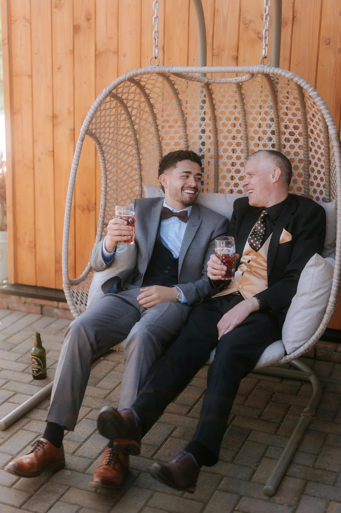 Two friends laughing together in a hanging wicker seat.