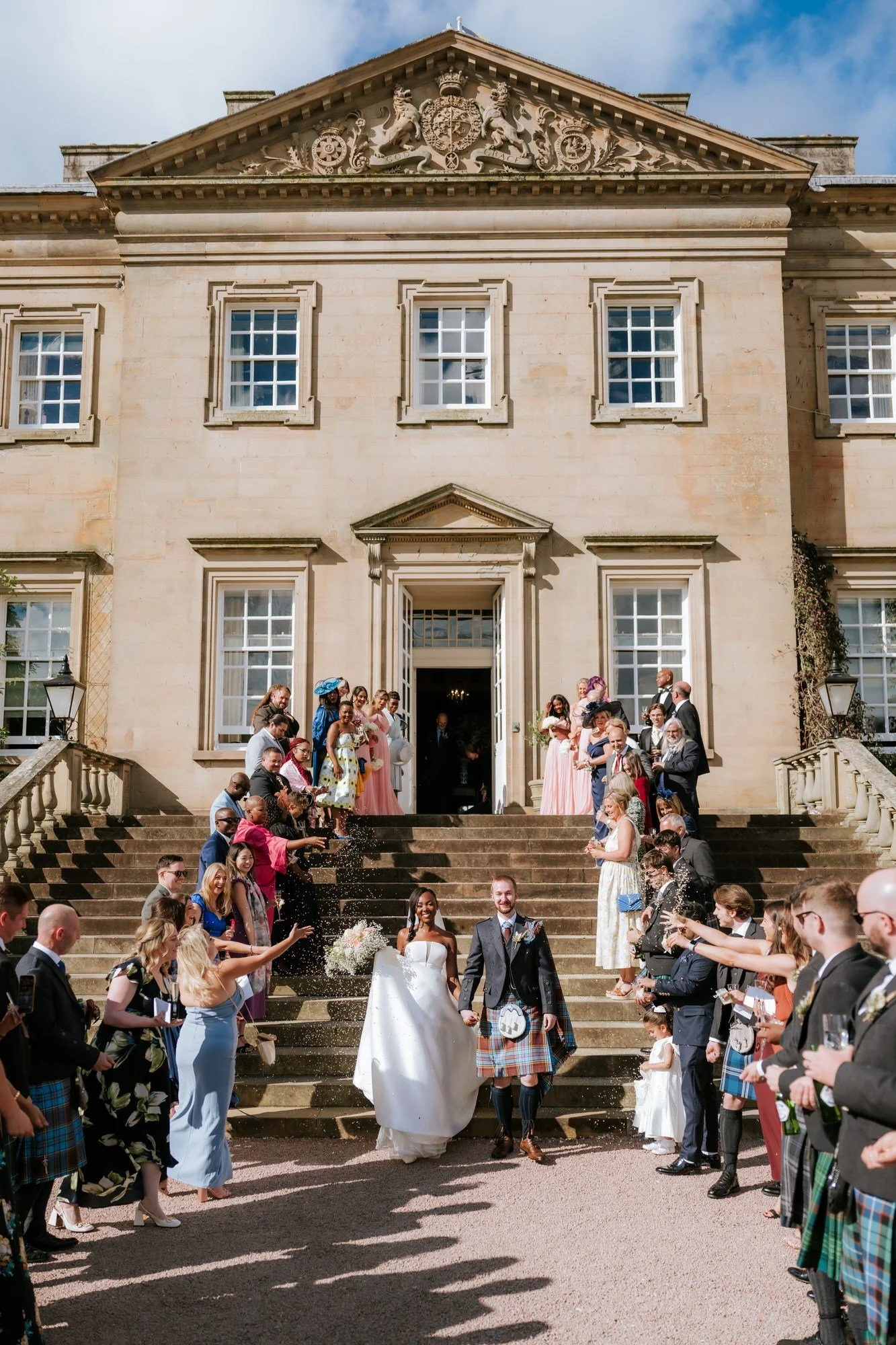 Kuda and Jamie walking through confetti on the grand steps of Dumfries House.