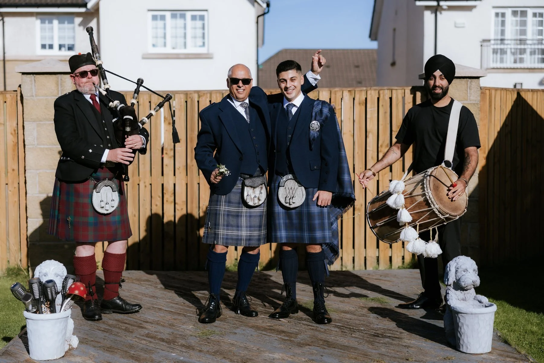 Wedding pipers and a drummer standing with two men in kilts outside before the ceremony.
