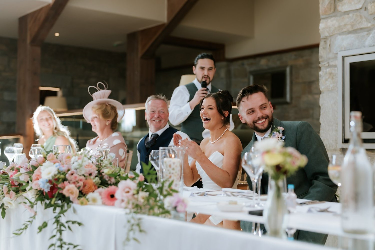 Lois and Dougie laughing at the top table while a groomsman gives his speech.