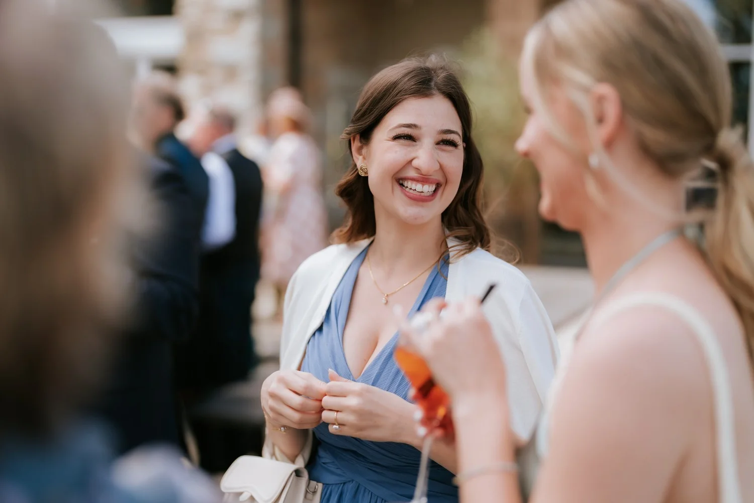 A wedding guest laughing with a bridesmaid outside in the sunshine.
