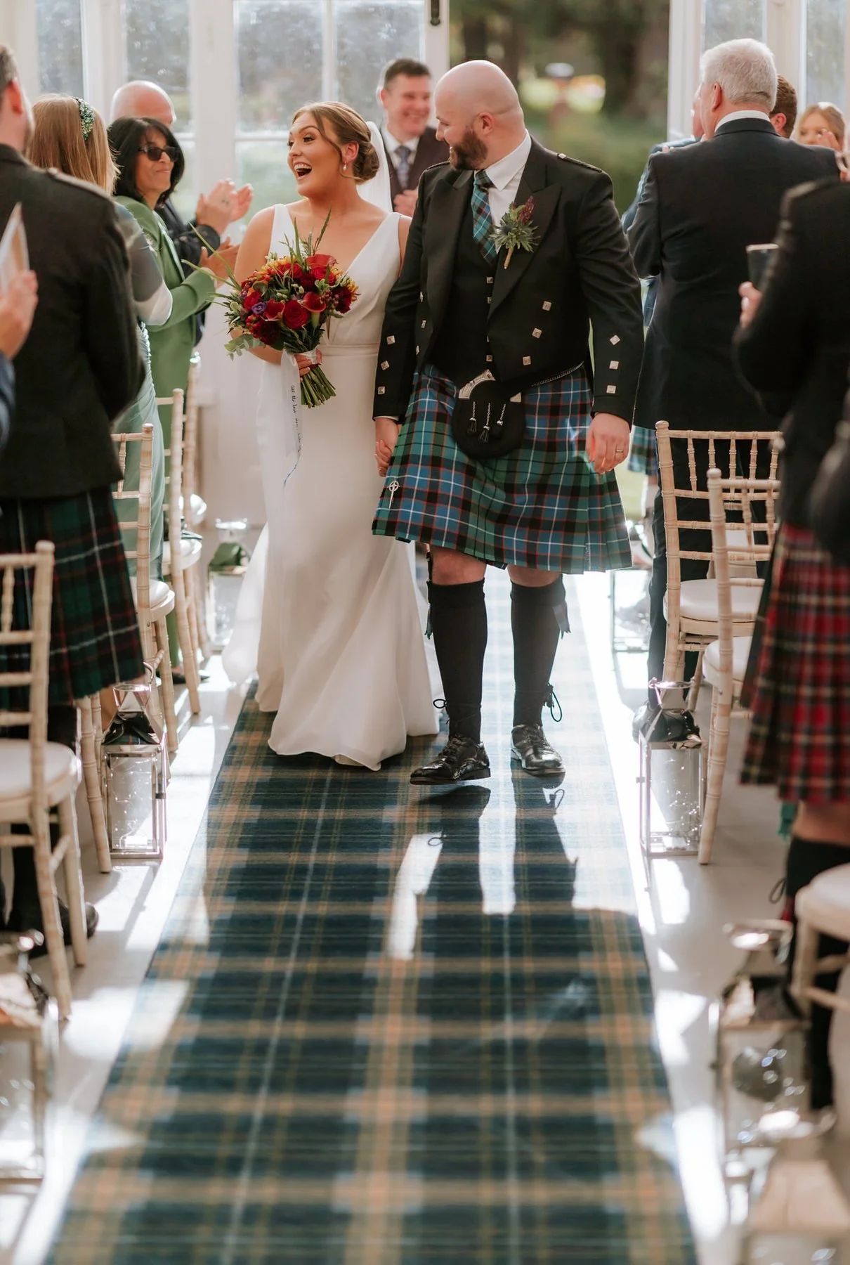 Kendall and Ewen smiling as they walk back along the conservatory aisle together.