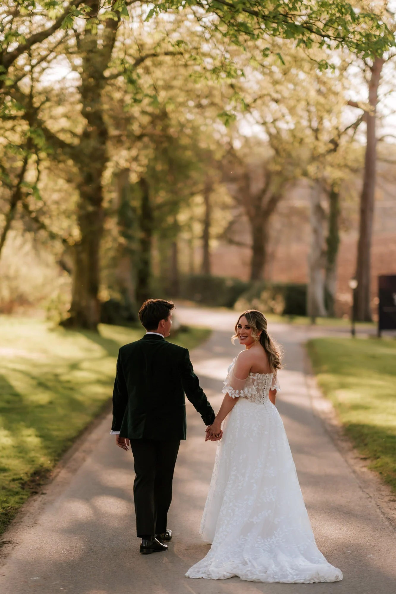 The couple walking along the tree-lined driveway and looking back.