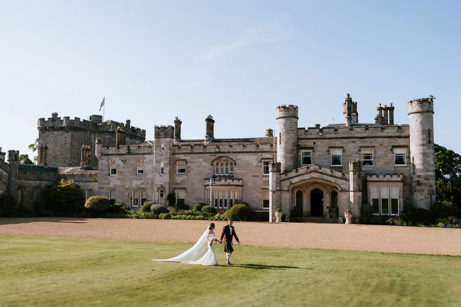 Kim and Kenneth walking hand in hand across the lawn in front of Dundas Castle.