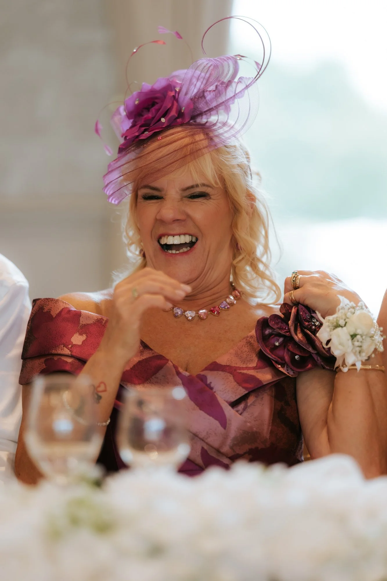 A wedding guest in a pink hat laughing during the reception at Glenbervie House.