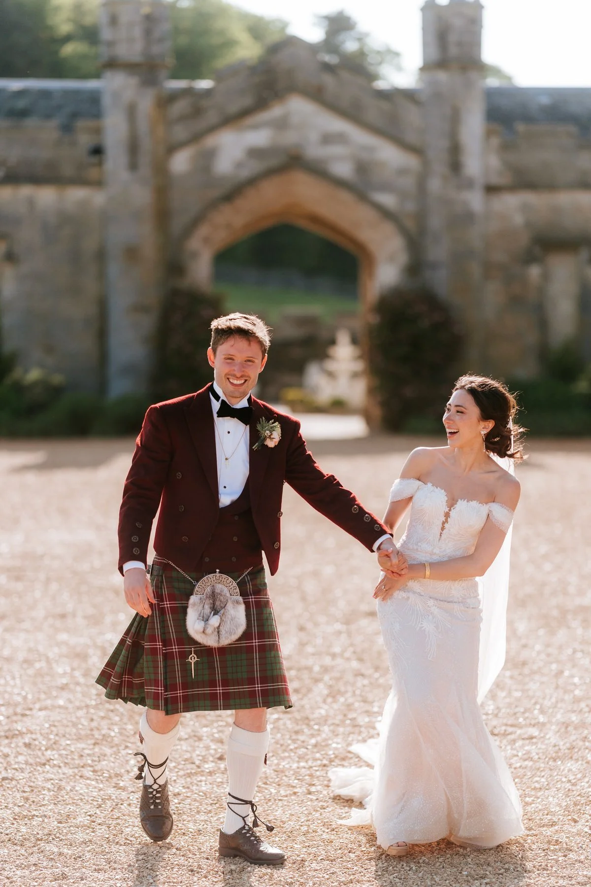 Kim and Kenneth laughing and holding hands as they walk away from the castle archway.