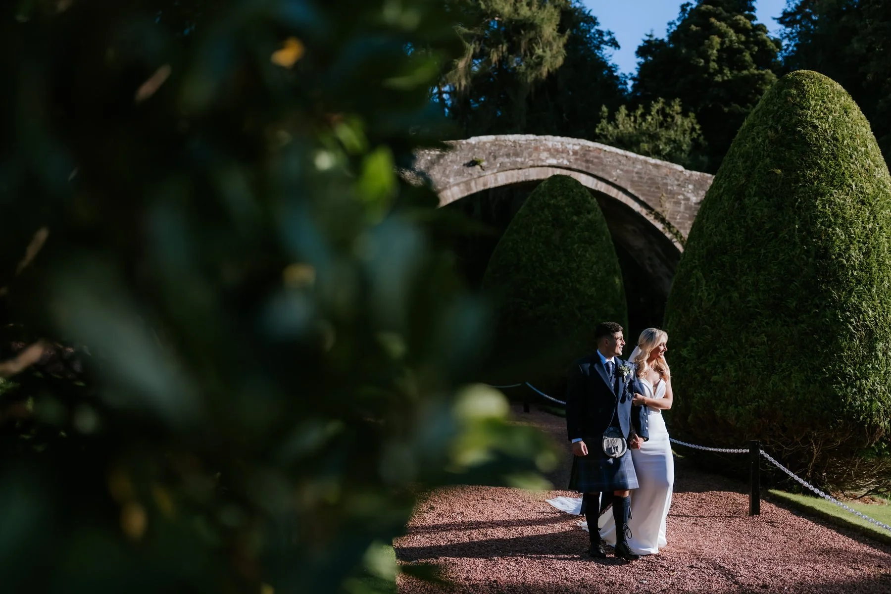 Lauren and Zen framed by garden foliage with the old stone bridge behind them.
