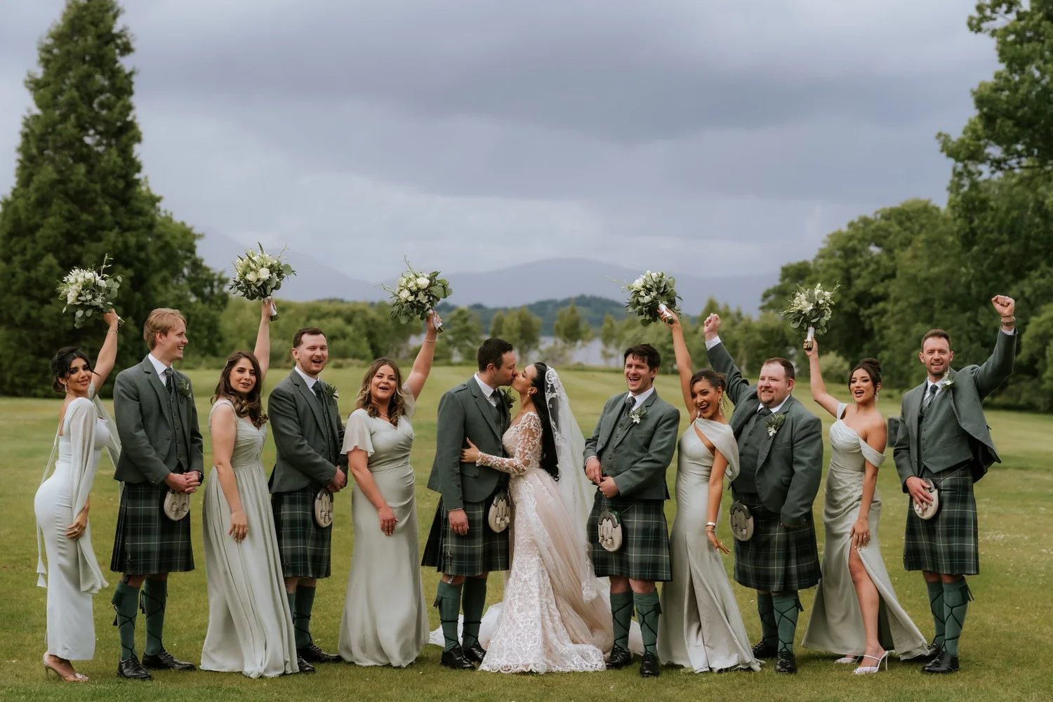 Cristina and Connor kissing as their wedding party cheers around them on the lawn.