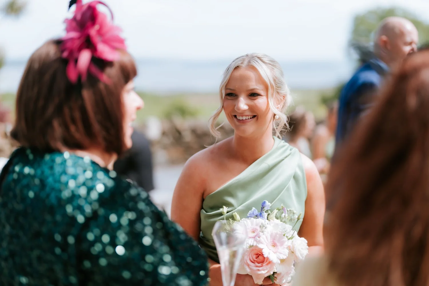 A bridesmaid smiling with her bouquet while chatting to guests at the drinks reception.