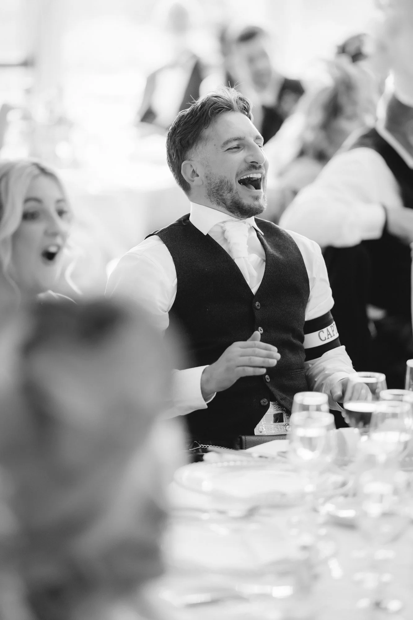 Black-and-white photograph of a laughing guest wearing a captain armband at Glenbervie House.