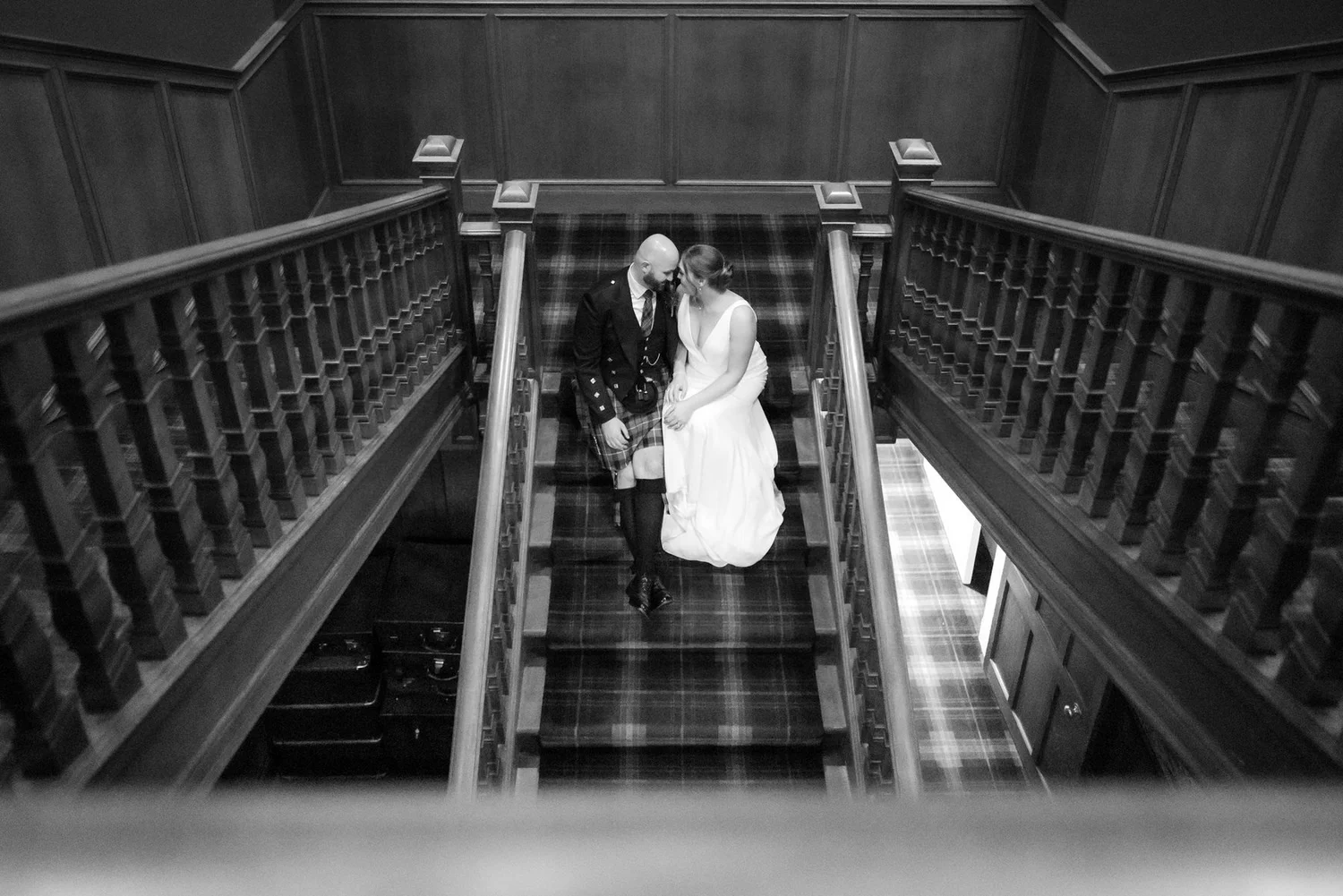 Black-and-white portrait of Kendall and Ewen sitting on the wooden staircase at SCHLOSS Roxburghe.