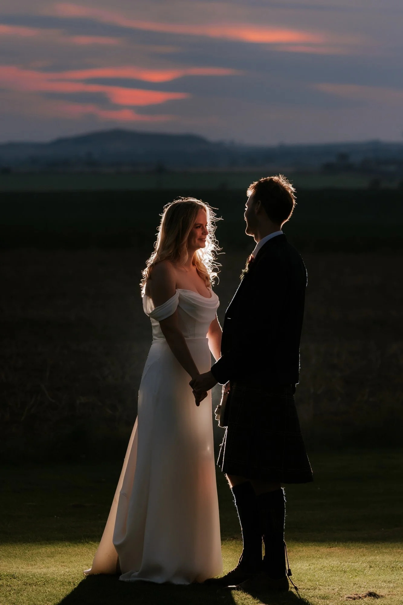 The couple face one another on the lawn at sunset, their outlines lit against the darkening landscape.