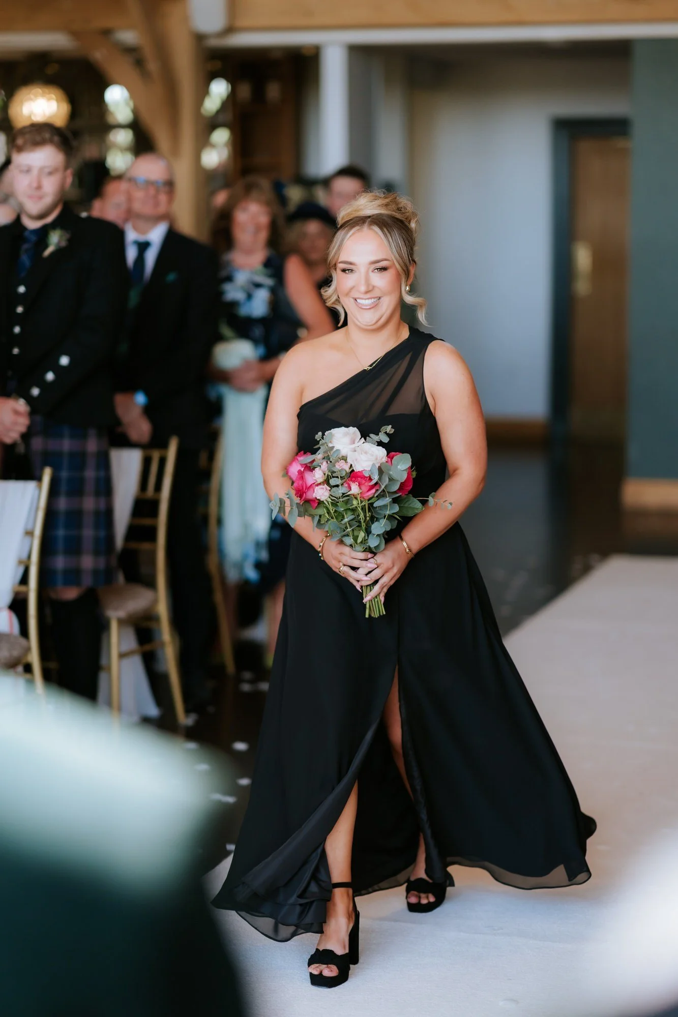 A smiling bridesmaid walking down the aisle with her bouquet.