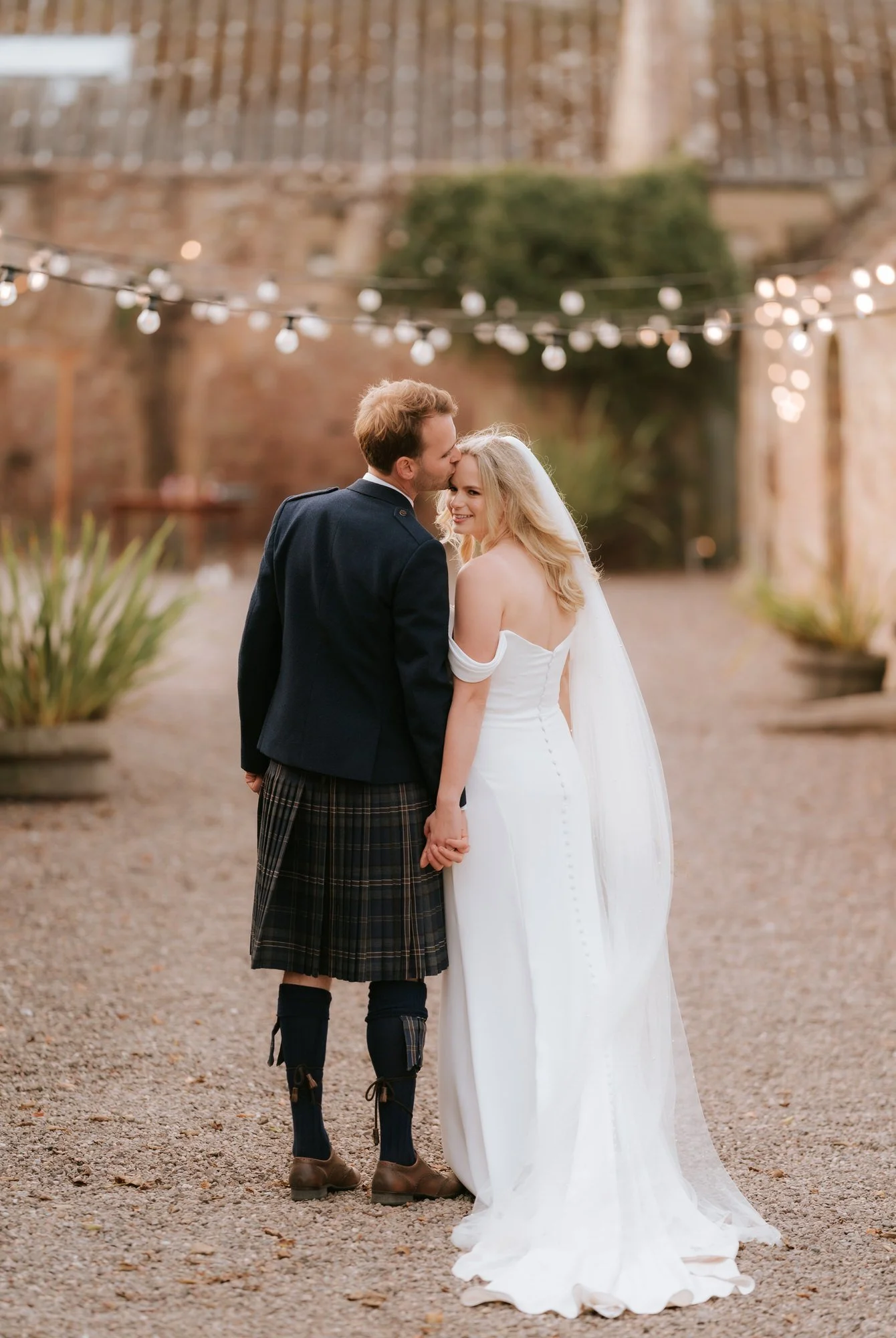 The couple turn towards each other in the courtyard, with the bride’s train spread across the gravel.