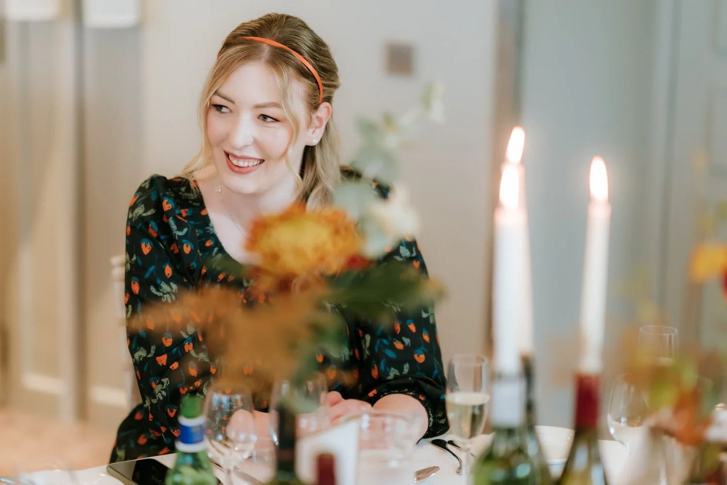A guest in a floral dress laughing beside the candles and autumn flowers.