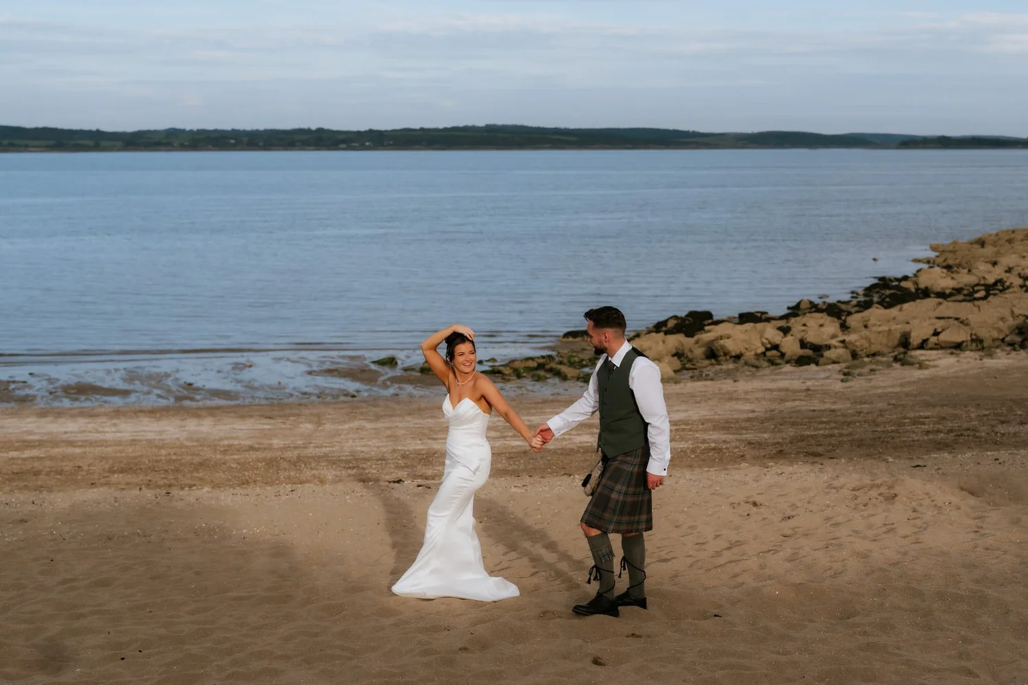Lois and Dougie holding hands on the sand during their evening beach photographs.