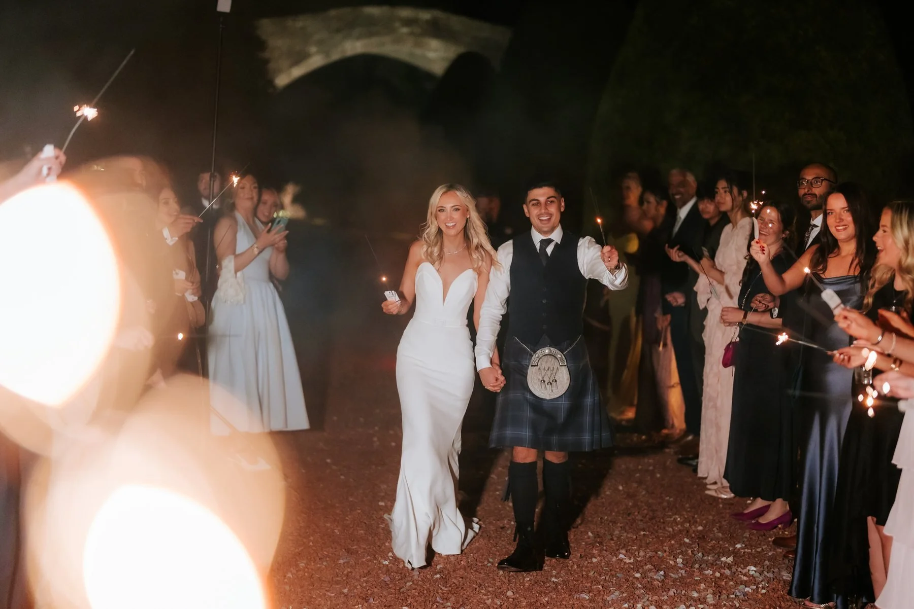 Lauren and Zen walking through a tunnel of sparklers held by their guests.