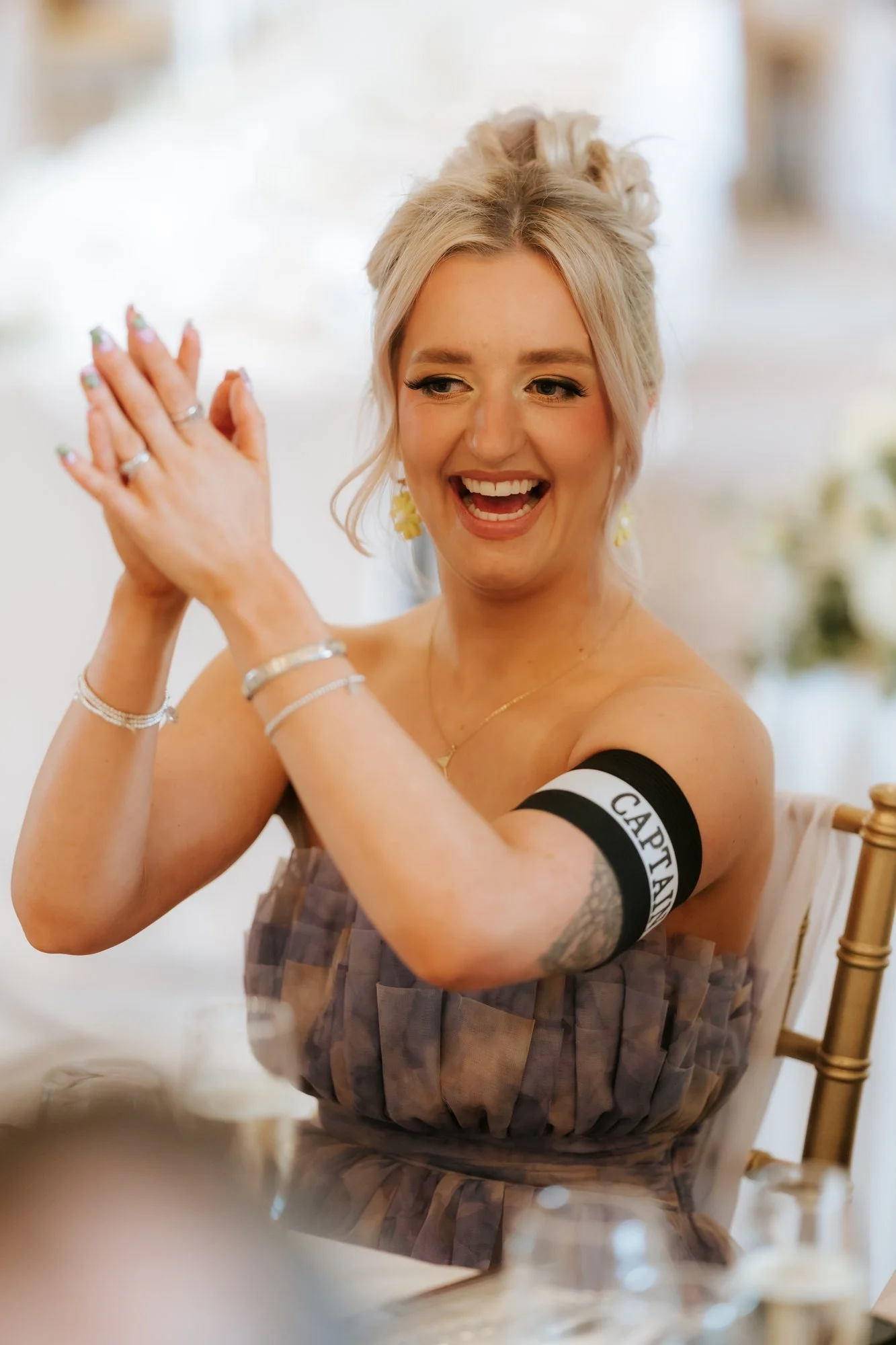 A wedding guest wearing a captain armband clapping at her table at Glenbervie House.