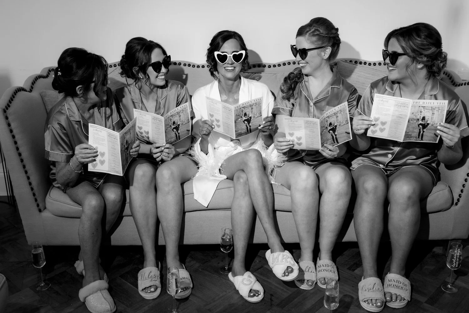 Lauren and her bridesmaids in robes and sunglasses reading wedding newspapers, photographed in black and white.