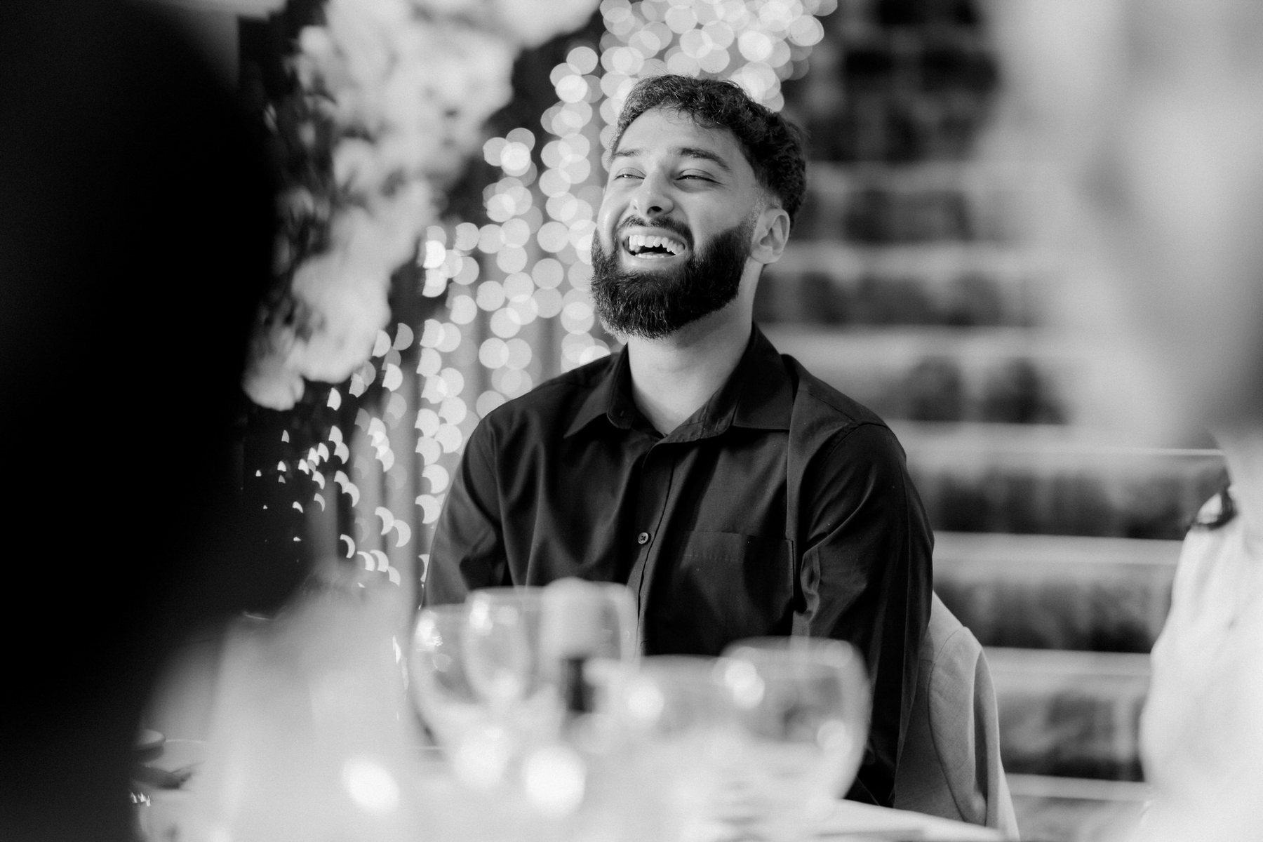 Black-and-white photograph of a guest laughing at the wedding reception table.