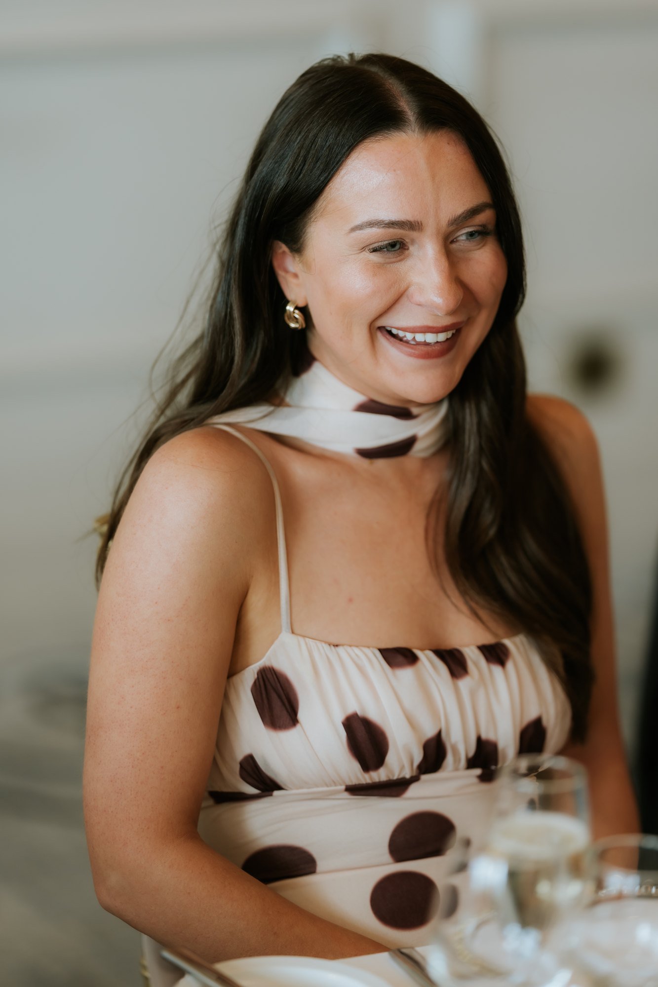 A smiling wedding guest in a cream and brown spotted dress at Glenbervie House.