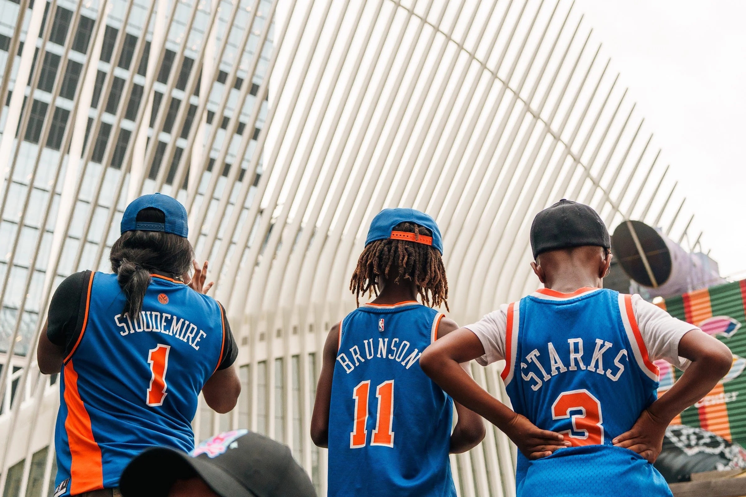 Fans in Knicks jerseys looking up toward One World Trade Center
