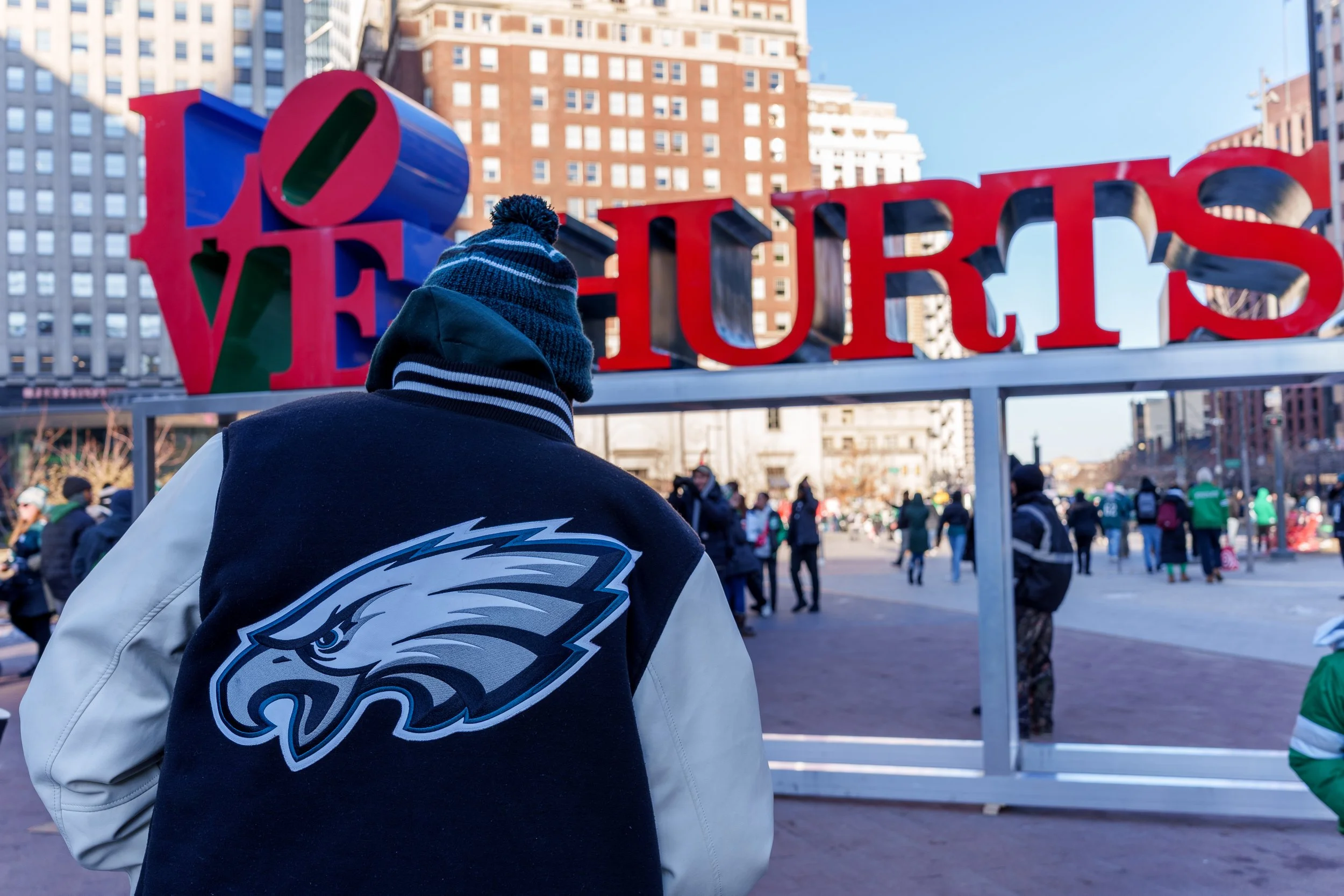 Fan in an Eagles varsity jacket facing the LOVE HURTS. sculpture