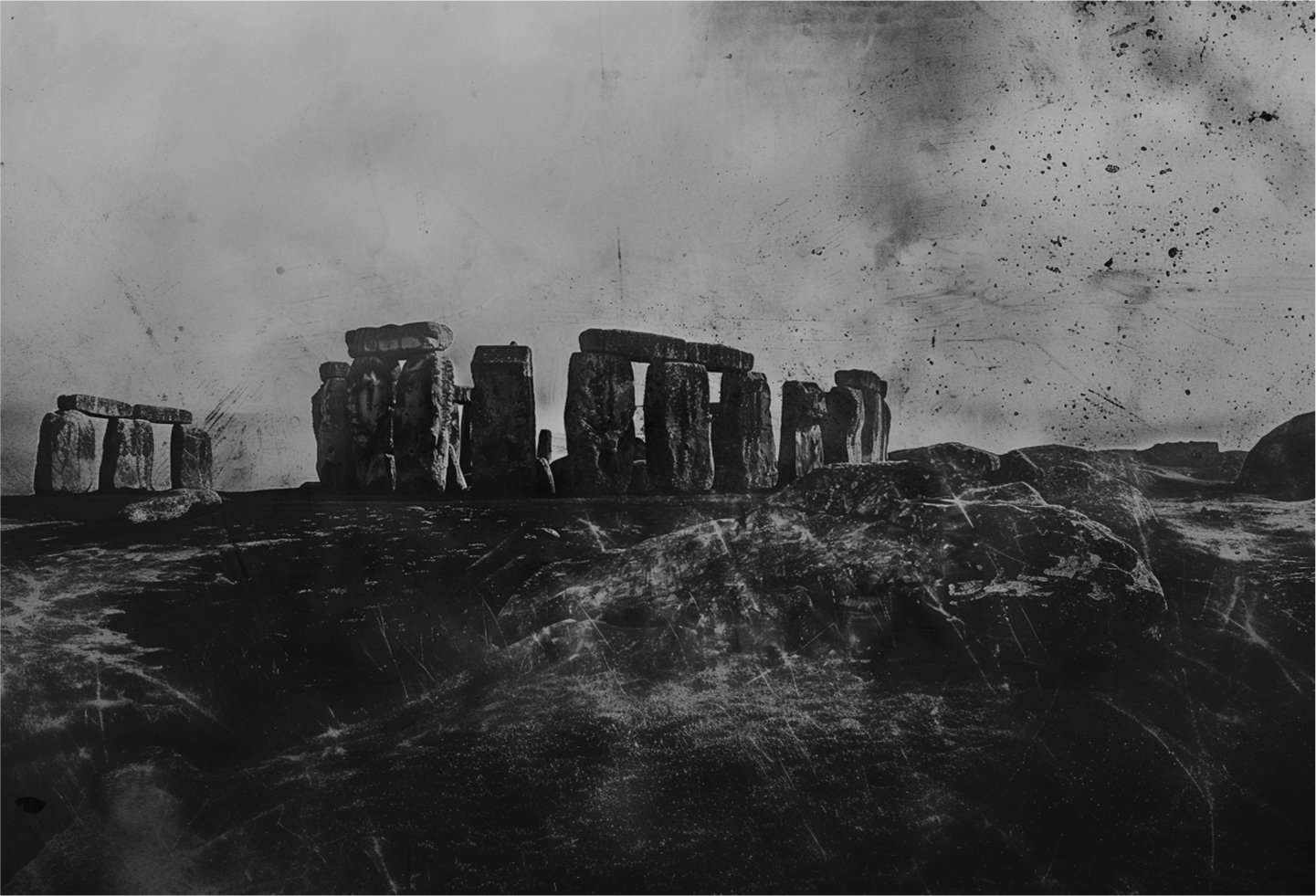 Black and white photo with film grain depicting a Stonehenge like arrangement of large stones a rocky barren style landscape.