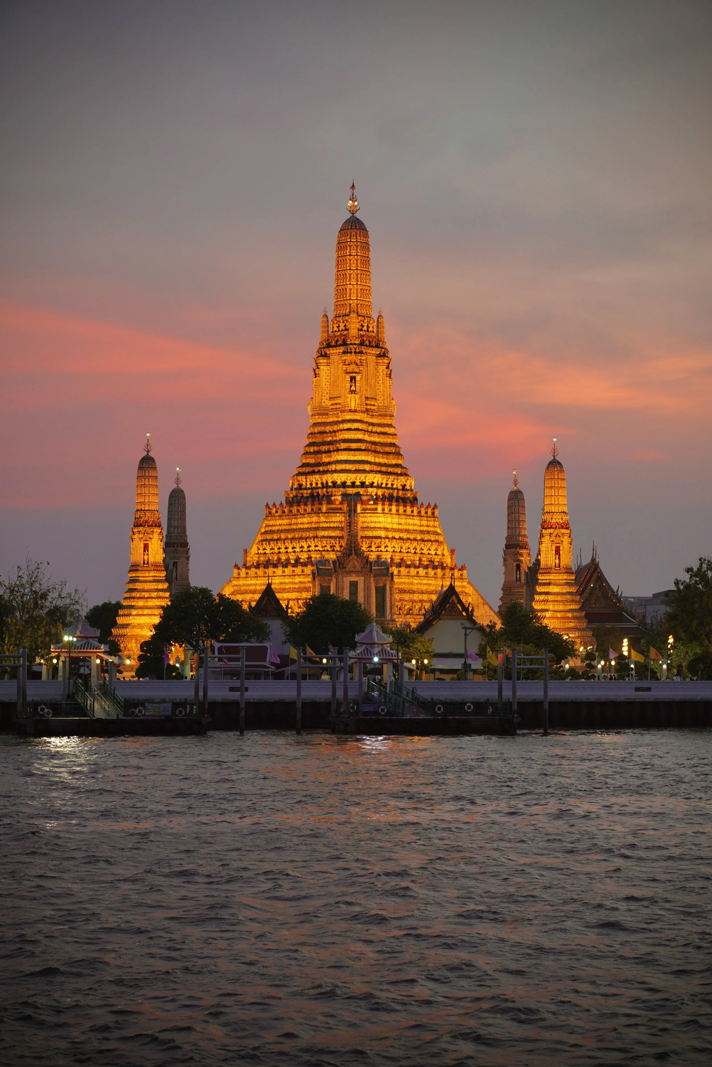 Bangkok — Wat Arun at golden hour from the river or a rooftop bar at night
