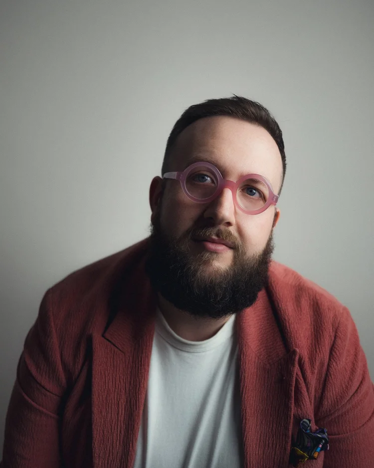 Hugo Herman-Wilson in a rust jacket and pink glasses, close-up