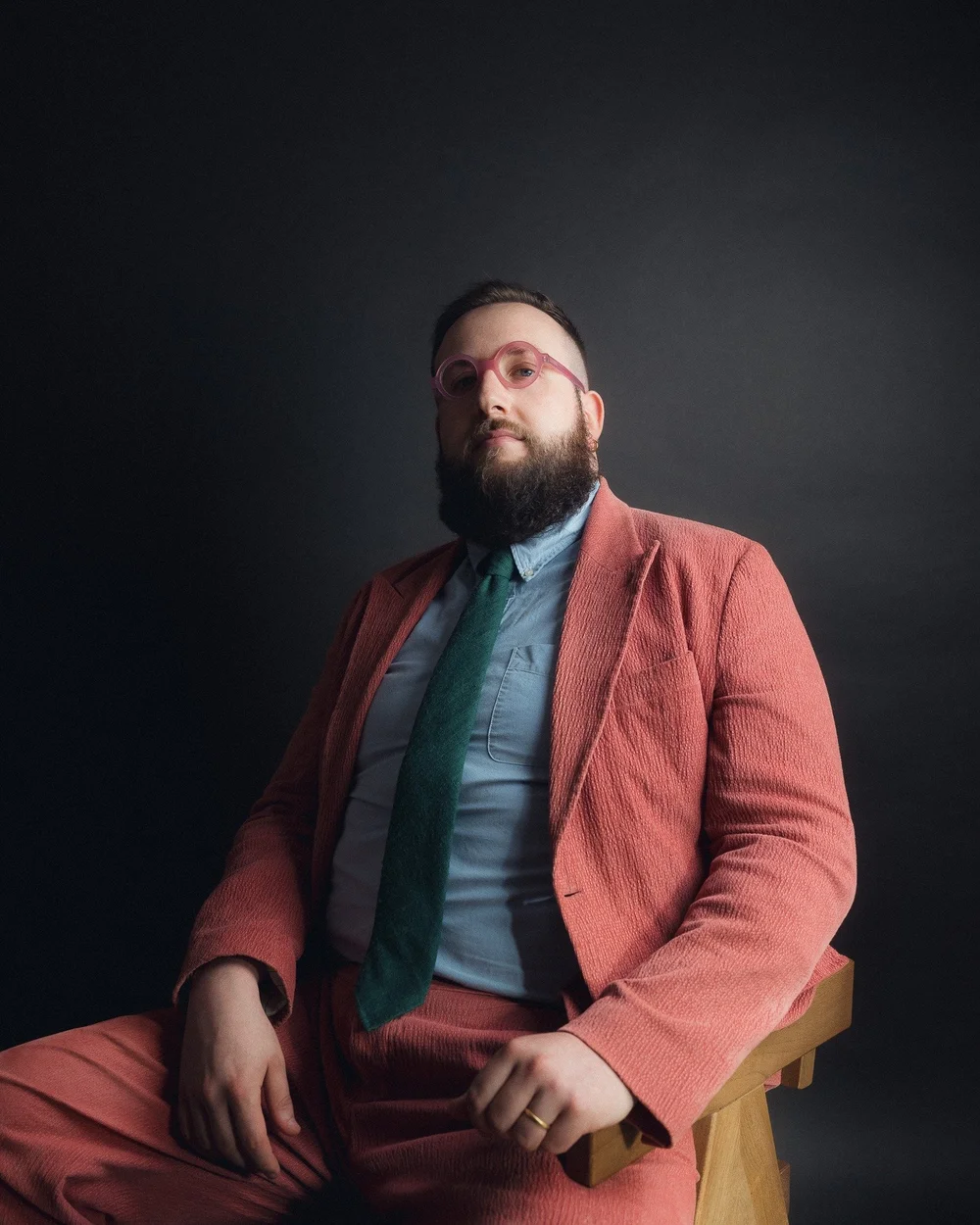Hugo Herman-Wilson, seated, in a suit and pink glasses