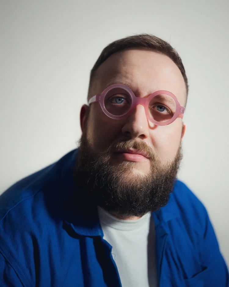 Hugo Herman-Wilson in a blue jacket and pink glasses, close-up