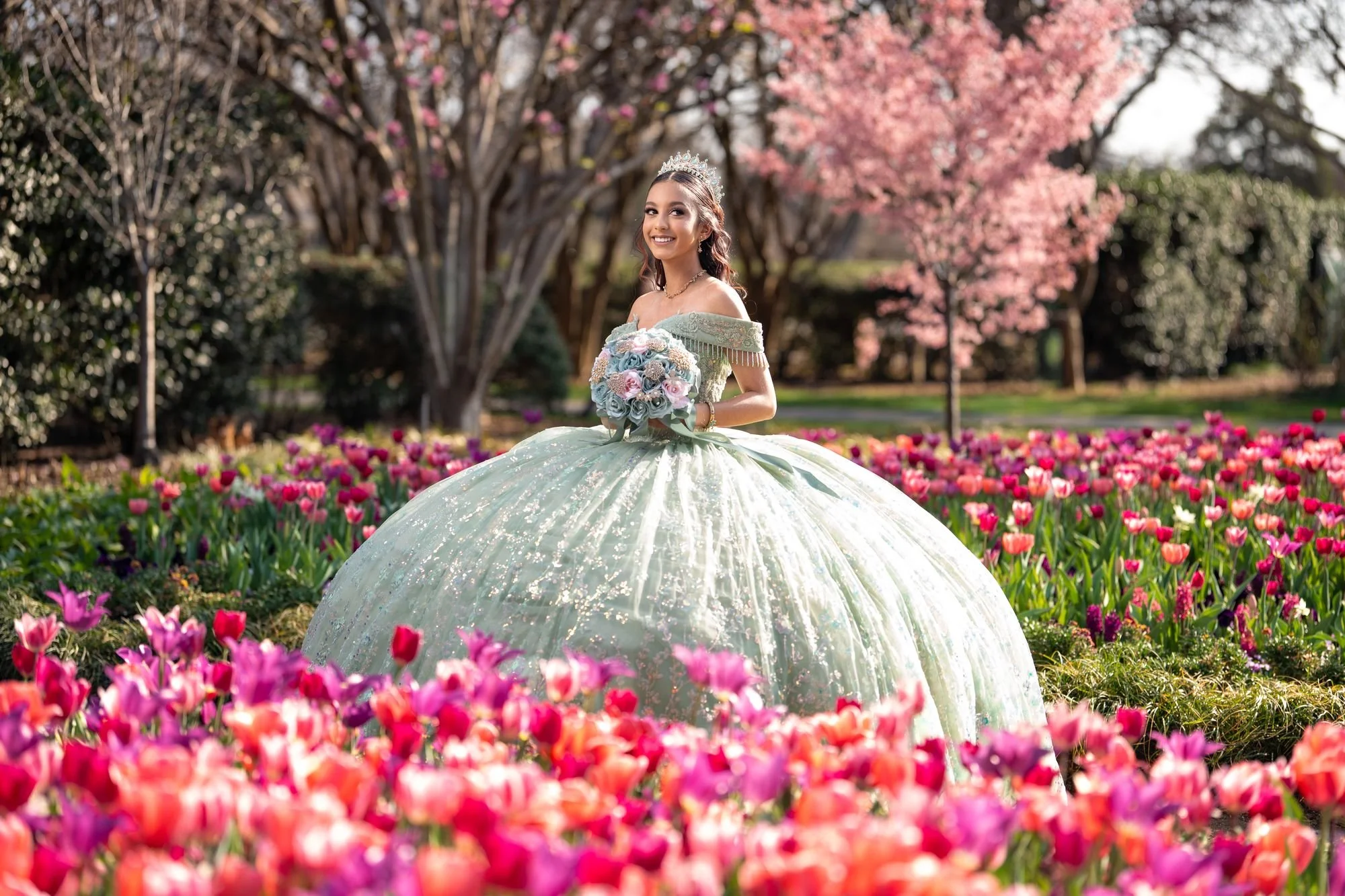 Quinceañera con vestido verde en un campo de tulipanes y flores de primavera