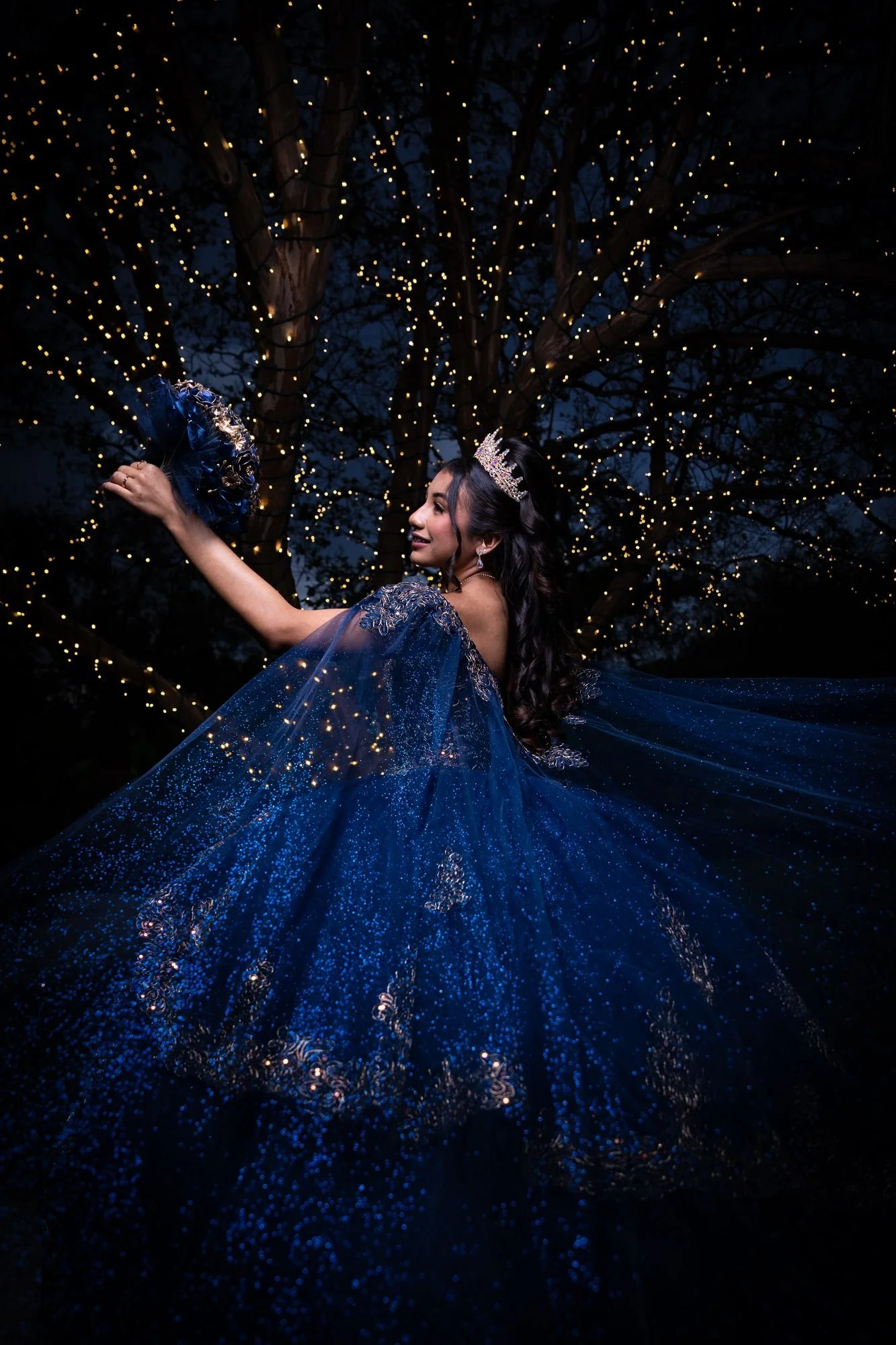 Quinceañera con vestido azul girando bajo luces colgantes de noche