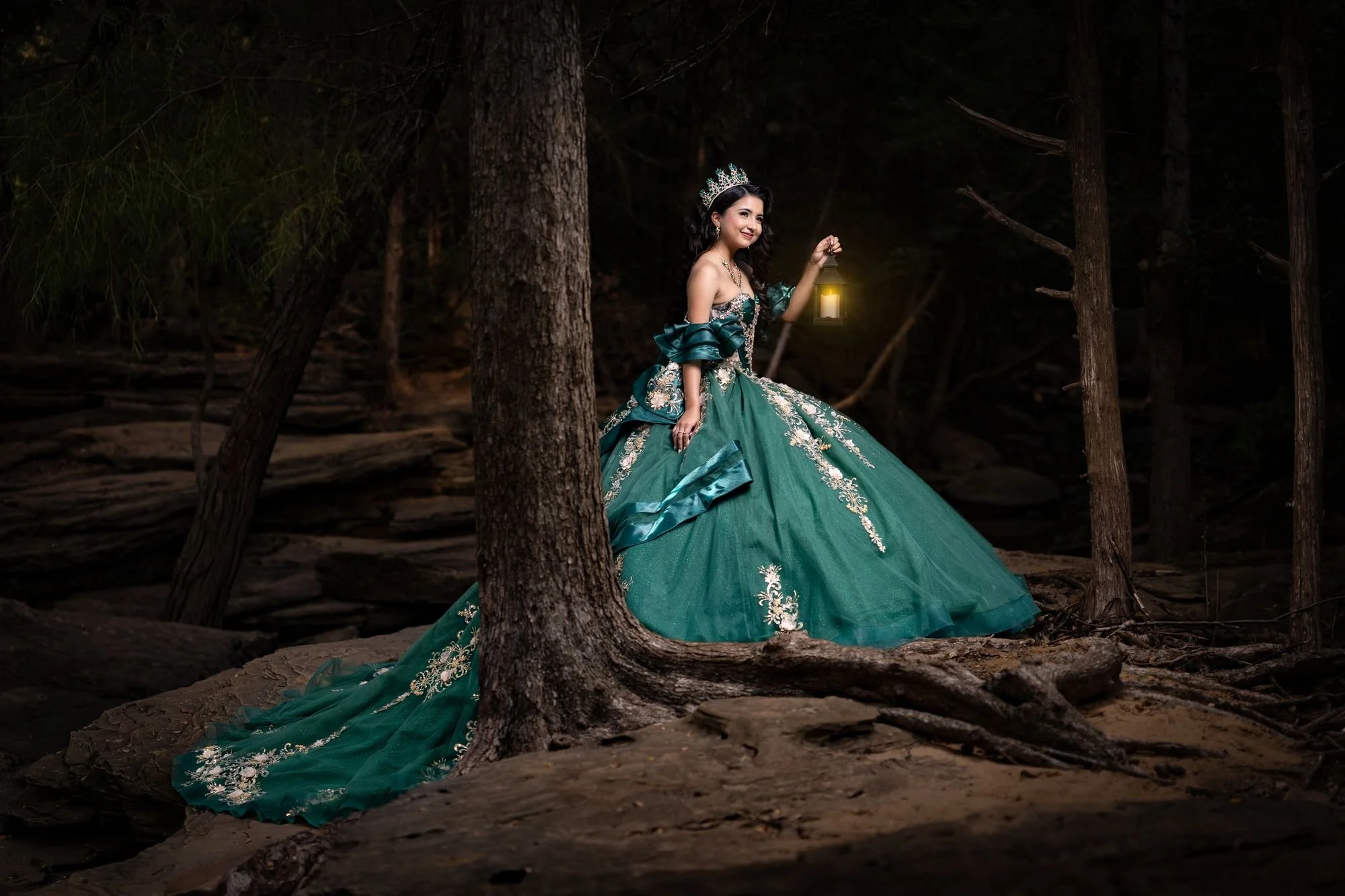 Quinceañera con vestido esmeralda sosteniendo un farol en un bosque encantado