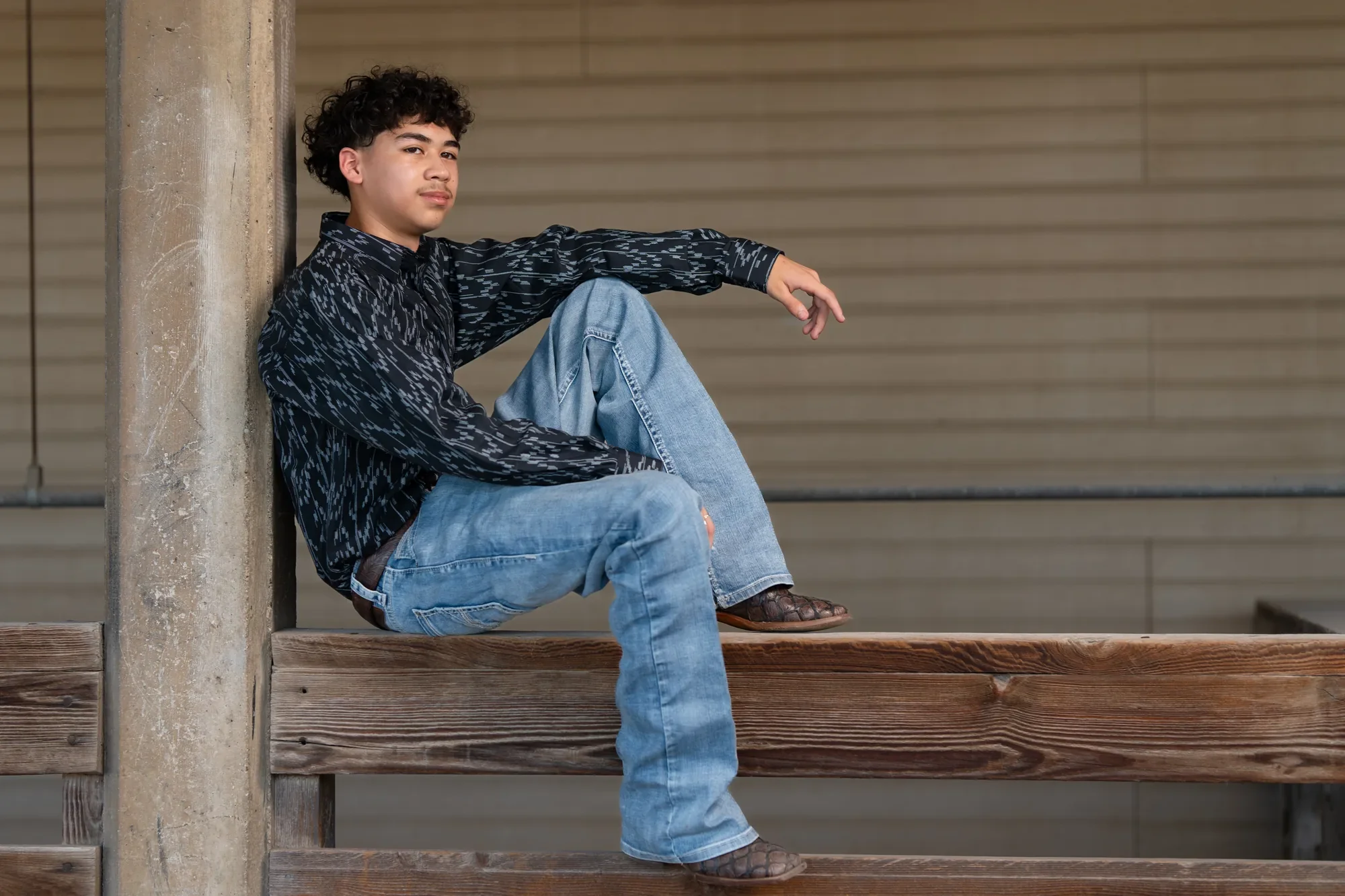 Quinceañero con atuendo vaquero formal y botas, fotografiado en una cerca de rancho en DFW