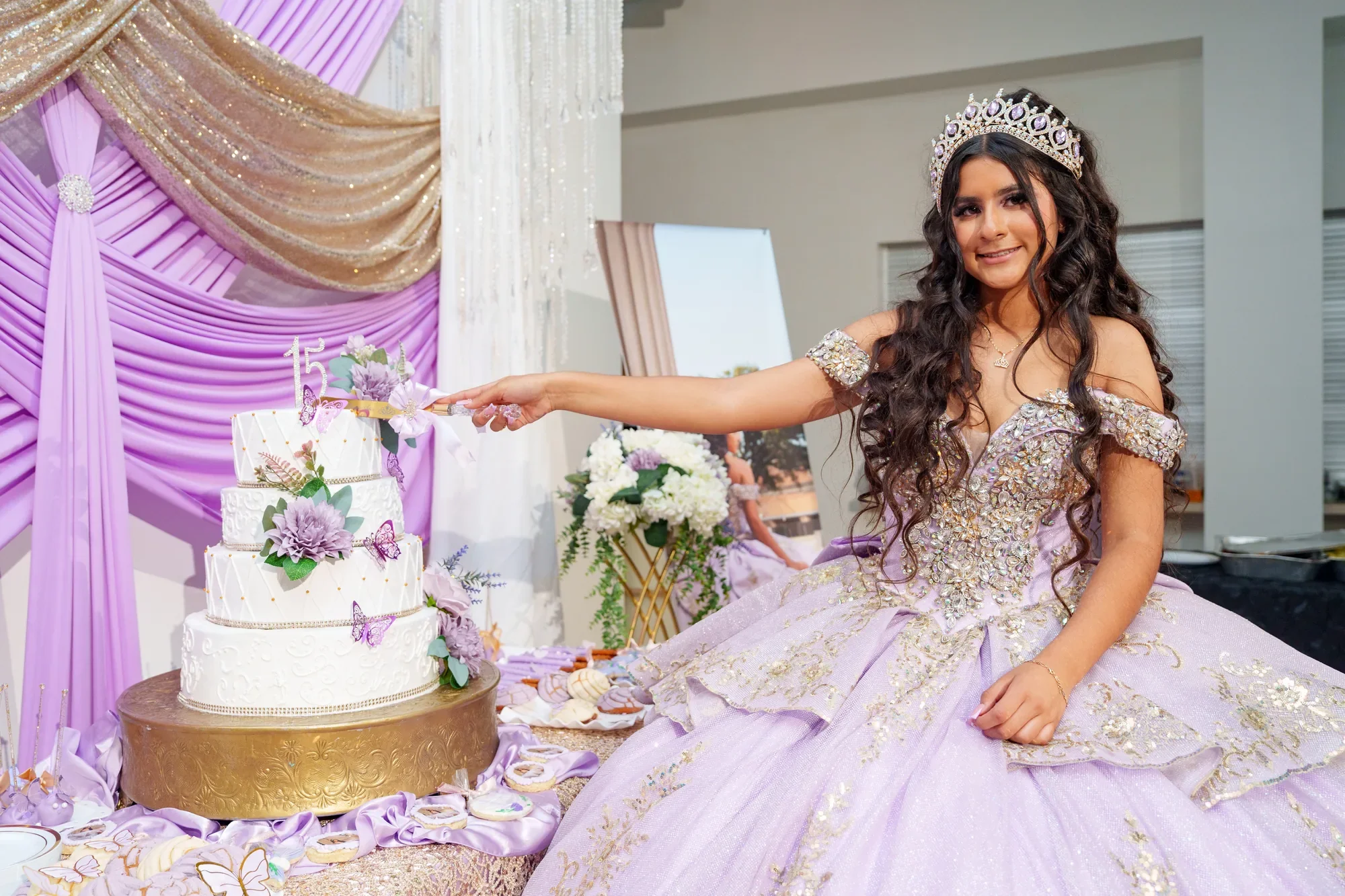 Una quinceañera con vestido lavanda y corona corta su pastel de tres pisos con mariposas