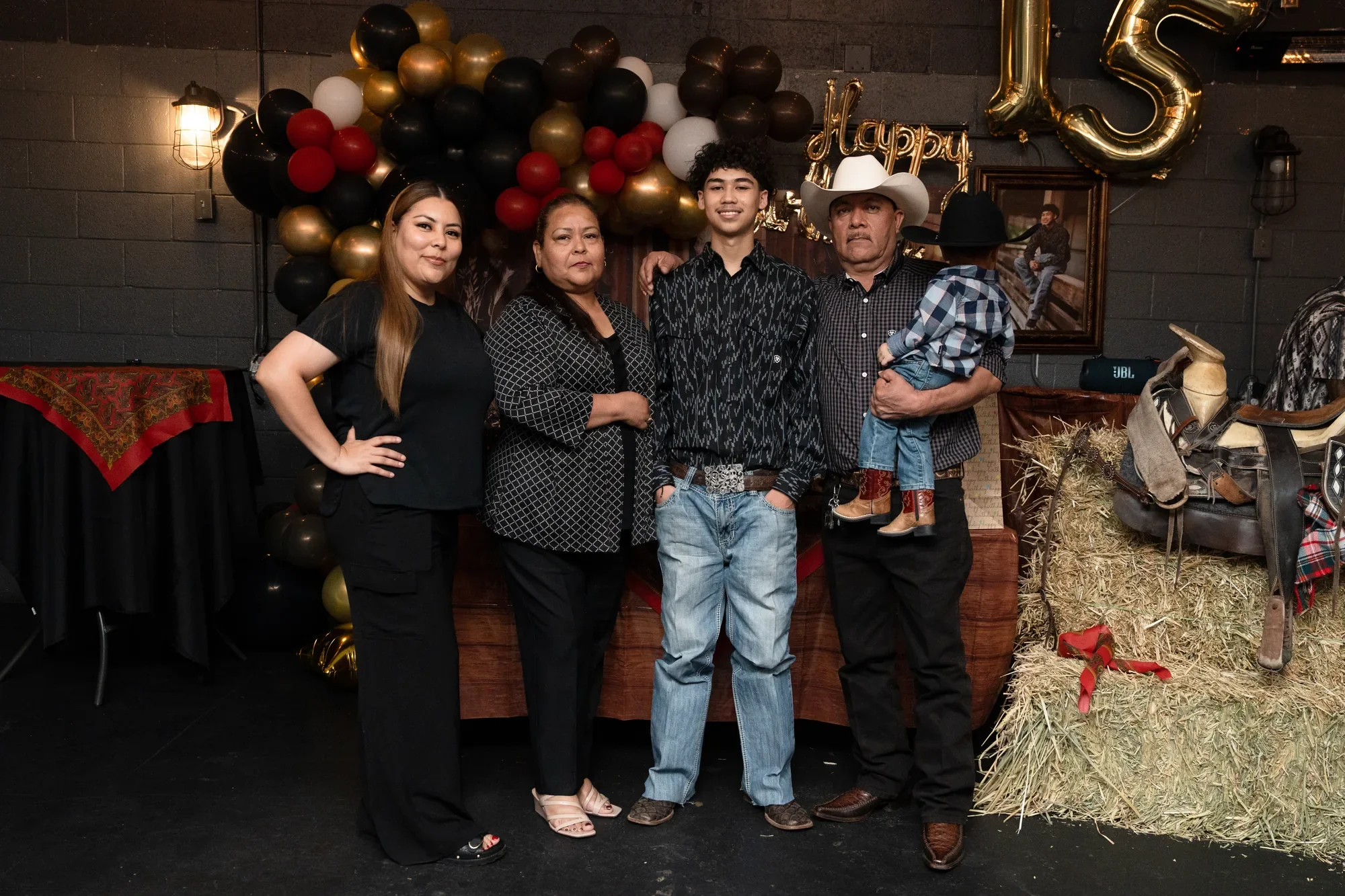 Familia celebrando el quinceañero vaquero de su hijo en DFW, con pacas de heno, silla de montar y globos dorados de 15
